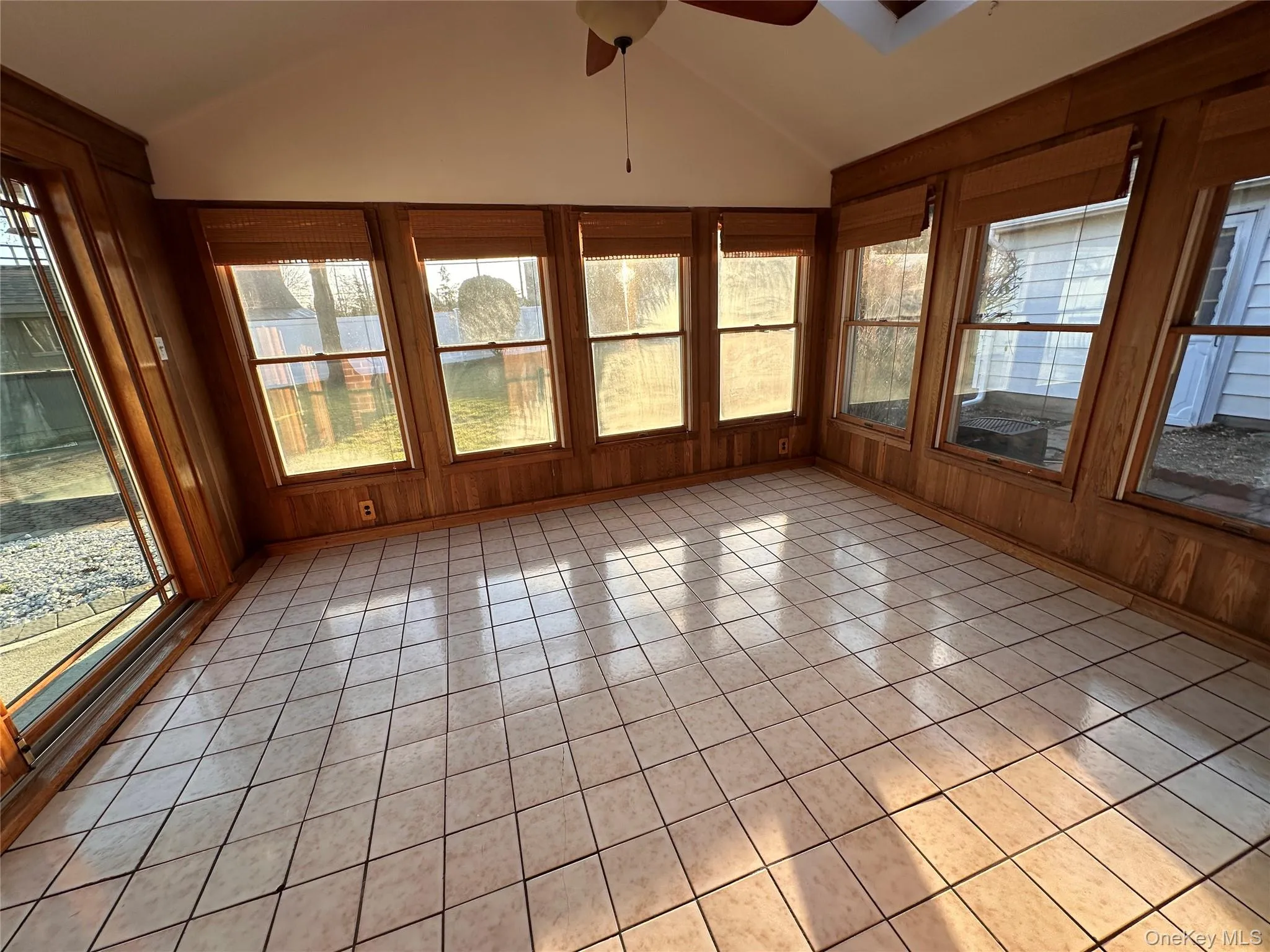 Unfurnished sunroom with lofted ceiling, wood walls, and tile patterned floors Unfurnished sunroom with lofted ceiling, wood walls, and tile patterned floors