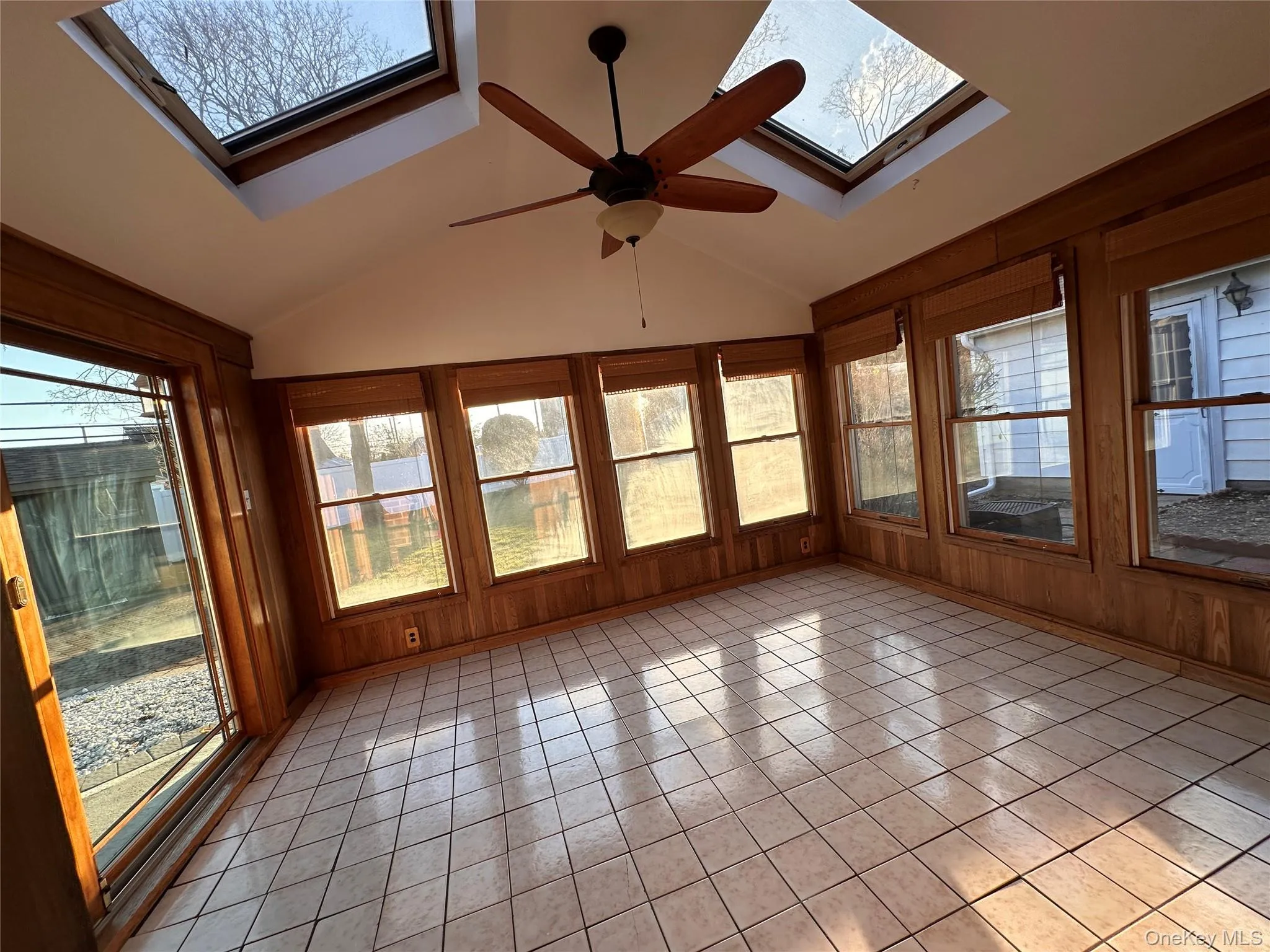 Unfurnished sunroom with plenty of natural light, a skylight, lofted ceiling, tile patterned flooring, and wooden walls Unfurnished sunroom with plenty of natural light, a skylight, lofted ceiling, tile patterned flooring, and wooden walls