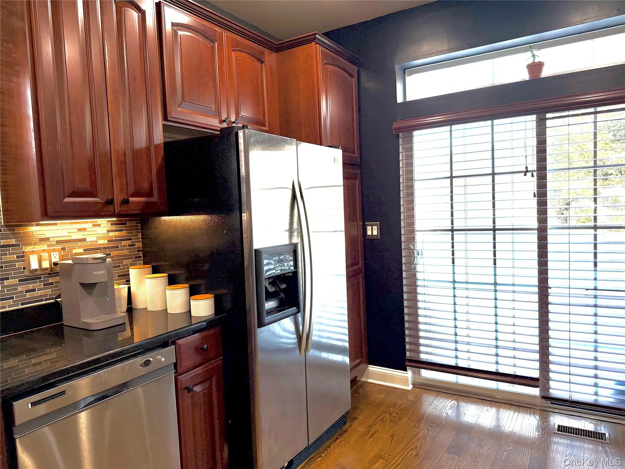 Kitchen with stainless steel appliances, decorative backsplash, dark stone countertops, and dark wood finished floors Kitchen with stainless steel appliances, decorative backsplash, dark stone countertops, and dark wood finished floors