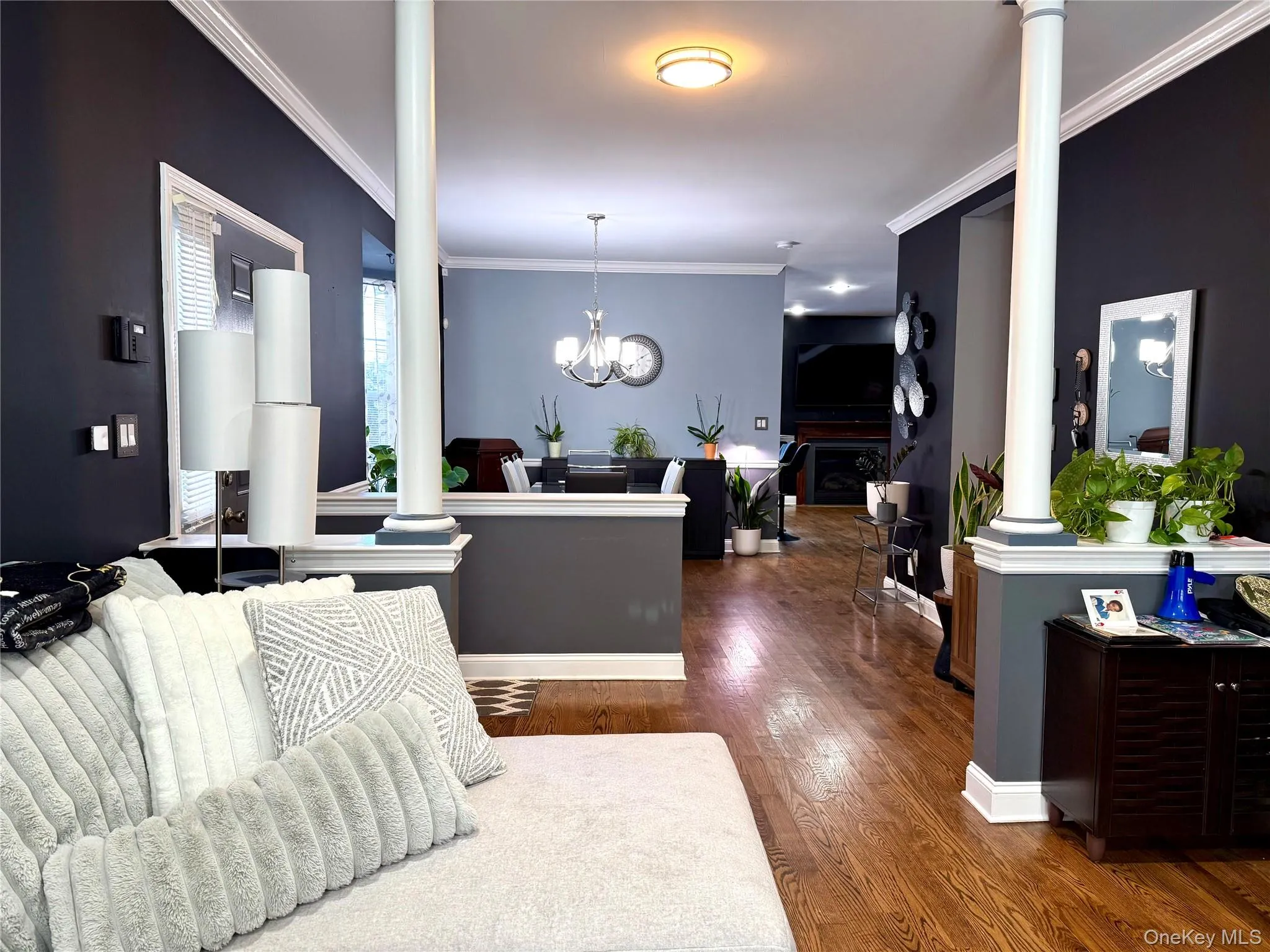 Living area with ornate columns, crown molding, dark wood finished floors, a fireplace, and a chandelier Living area with ornate columns, crown molding, dark wood finished floors, a fireplace, and a chandelier