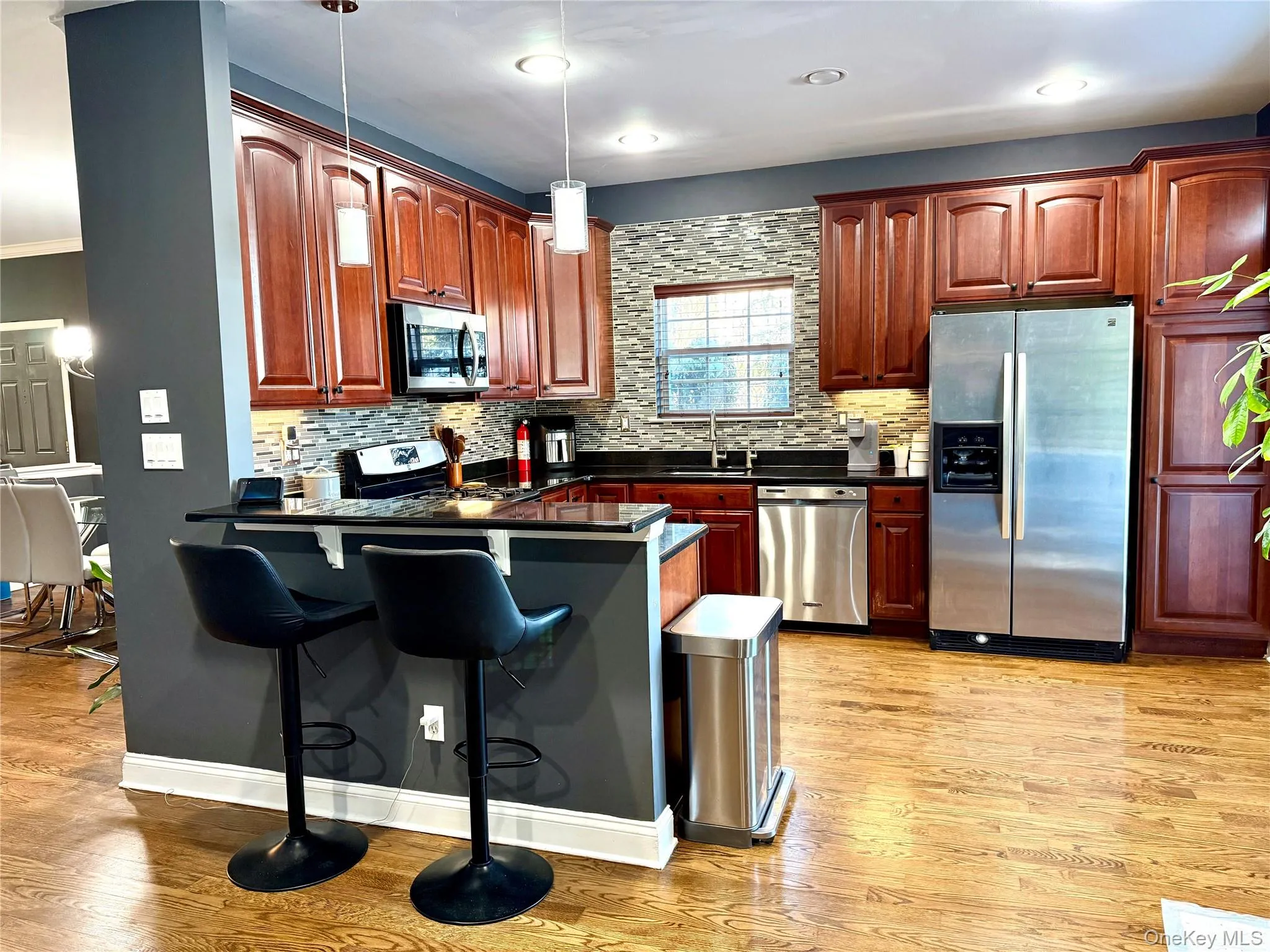 Kitchen featuring appliances with stainless steel finishes, a kitchen bar, pendant lighting, a peninsula, and decorative backsplash Kitchen featuring appliances with stainless steel finishes, a kitchen bar, pendant lighting, a peninsula, and decorative backsplash