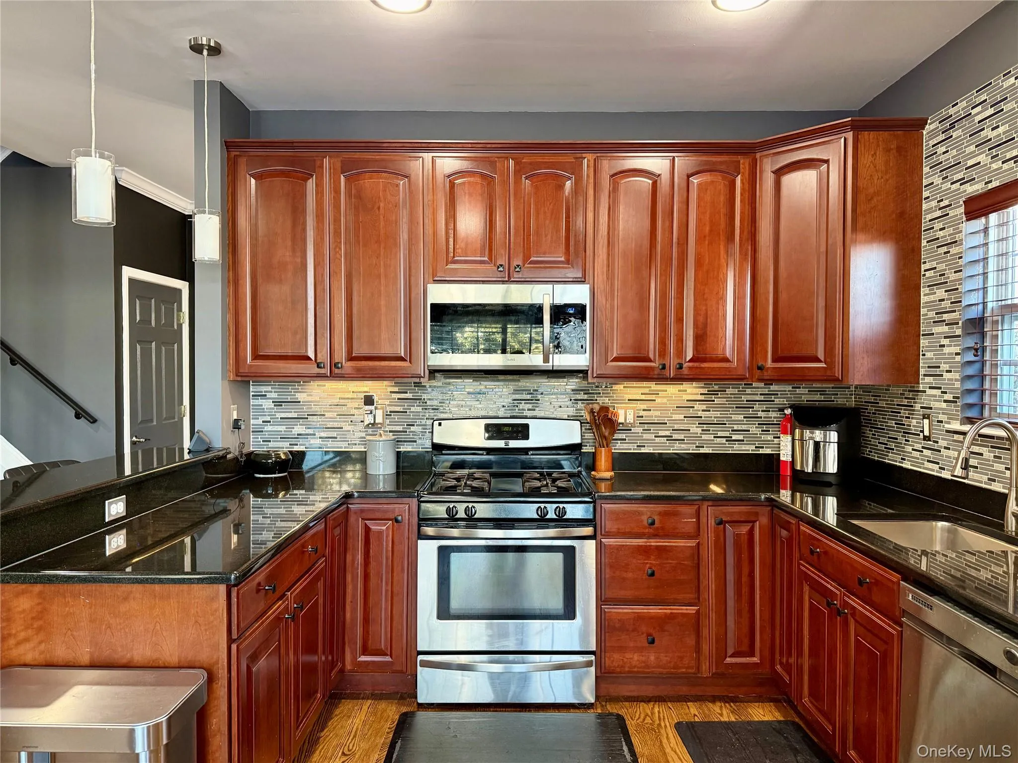 Kitchen featuring appliances with stainless steel finishes, dark stone counters, hanging light fixtures, and light wood-style floors Kitchen featuring appliances with stainless steel finishes, dark stone counters, hanging light fixtures, and light wood-style floors