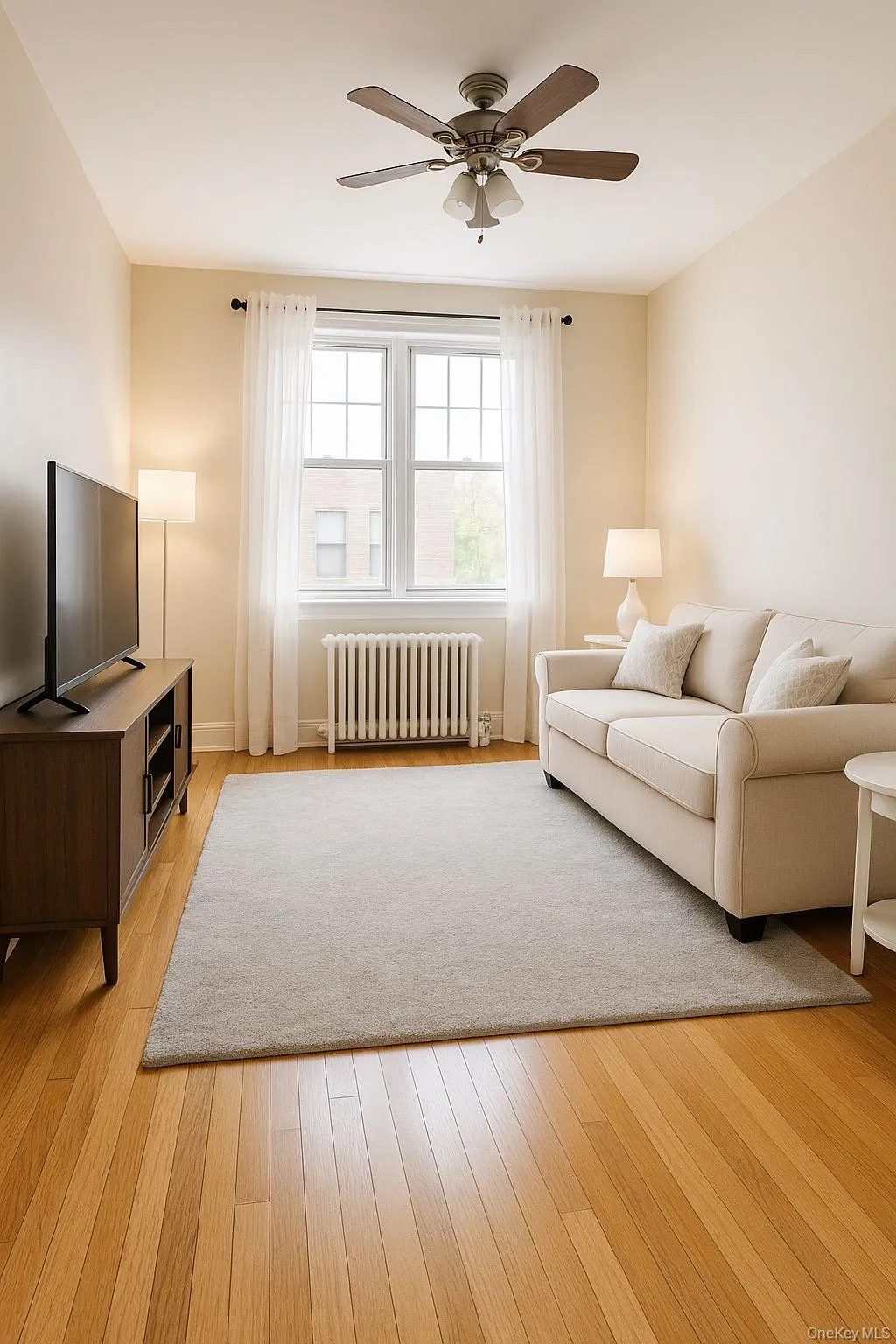 Living area featuring radiator heating unit, a ceiling fan, and light wood-style flooring Living area featuring radiator heating unit, a ceiling fan, and light wood-style flooring