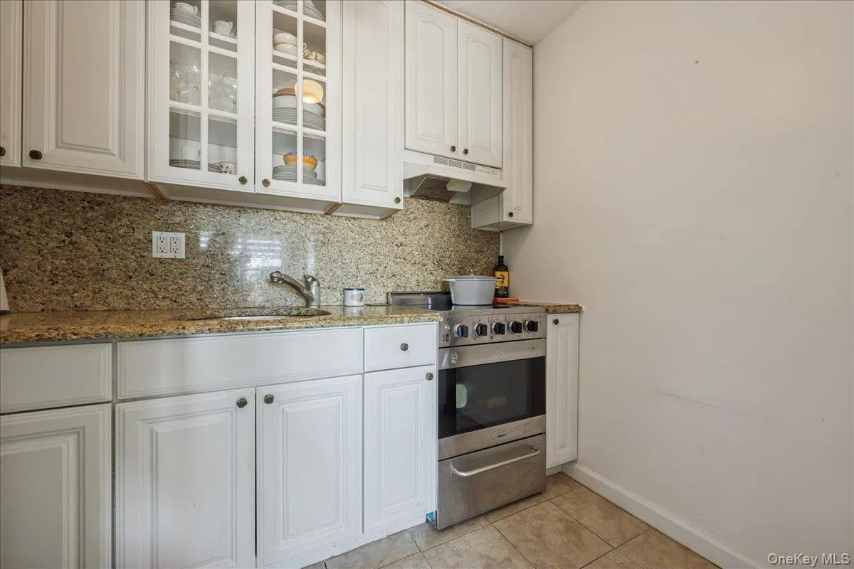 Kitchen featuring white cabinets, stainless steel stove, under cabinet range hood, and tasteful backsplash Kitchen featuring white cabinets, stainless steel stove, under cabinet range hood, and tasteful backsplash