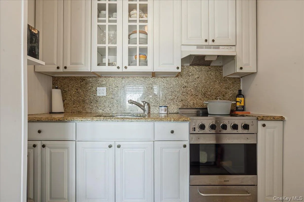 Kitchen featuring stainless steel stove, light stone counters, glass insert cabinets, and white cabinetry Kitchen featuring stainless steel stove, light stone counters, glass insert cabinets, and white cabinetry