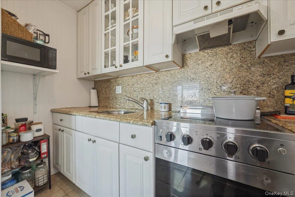 Kitchen with stainless steel range with electric cooktop, under cabinet range hood, white cabinetry, black microwave, and light stone counters Kitchen with stainless steel range with electric cooktop, under cabinet range hood, white cabinetry, black microwave, and light stone counters