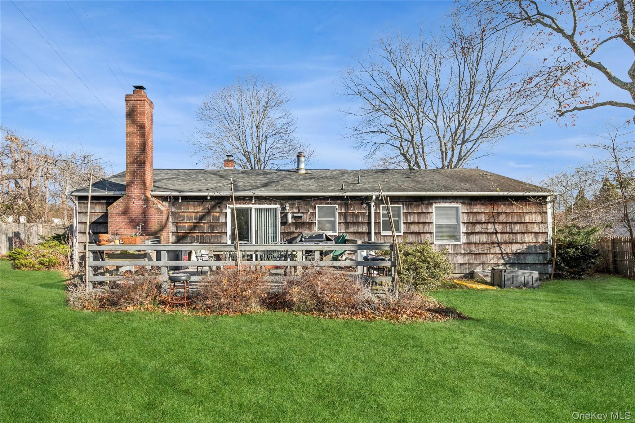 Back of property with a chimney, a deck, and a shingled roof Back of property with a chimney, a deck, and a shingled roof