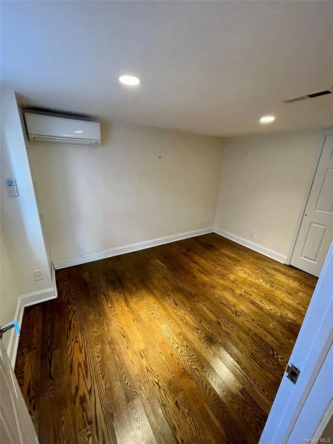 Empty room featuring dark wood-style flooring, recessed lighting, and a wall mounted air conditioner Empty room featuring dark wood-style flooring, recessed lighting, and a wall mounted air conditioner