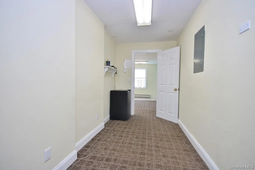Corridor with electric panel, dark colored carpet, and a baseboard heating unit Corridor with electric panel, dark colored carpet, and a baseboard heating unit