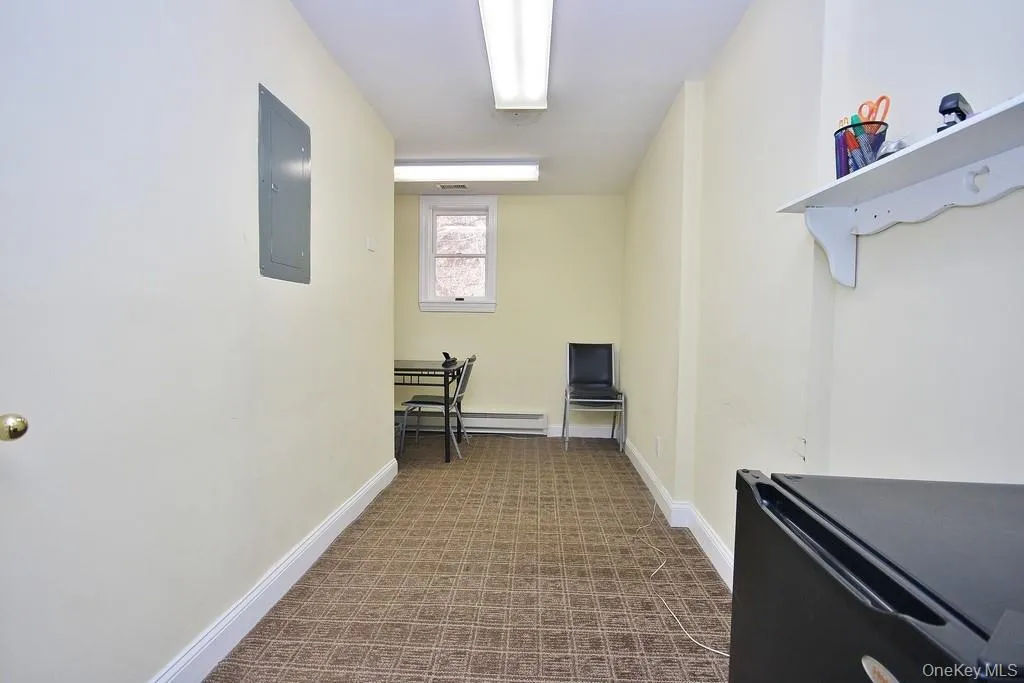 Hallway with electric panel, carpet, and a baseboard heating unit Hallway with electric panel, carpet, and a baseboard heating unit