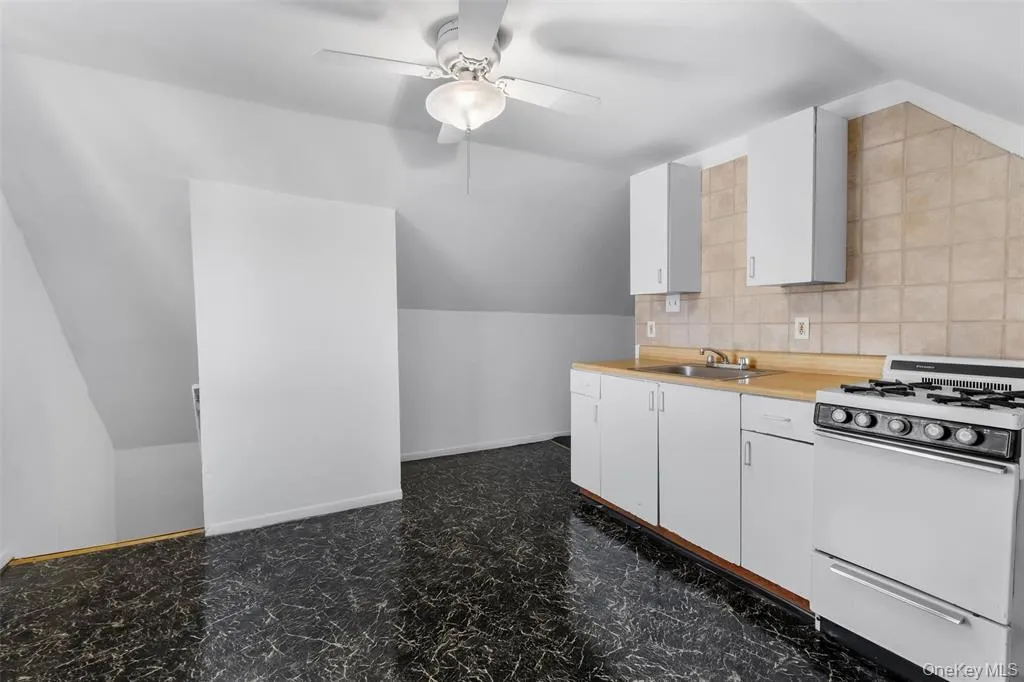 Kitchen featuring lofted ceiling, white cabinets, ceiling fan, tasteful backsplash, and range Kitchen featuring lofted ceiling, white cabinets, ceiling fan, tasteful backsplash, and range