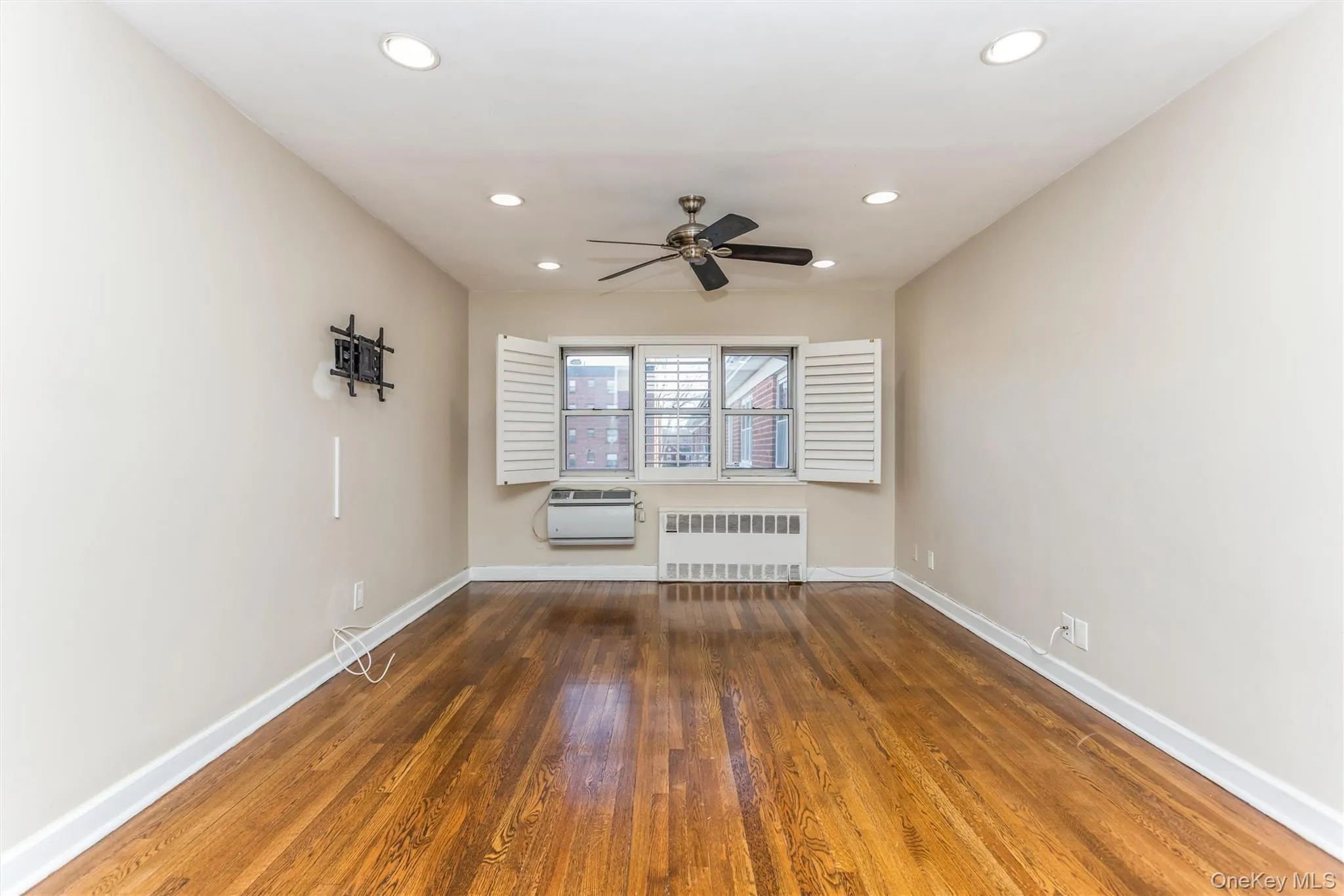 Empty room featuring dark wood finished floors, radiator heating unit, recessed lighting, and ceiling fan Empty room featuring dark wood finished floors, radiator heating unit, recessed lighting, and ceiling fan