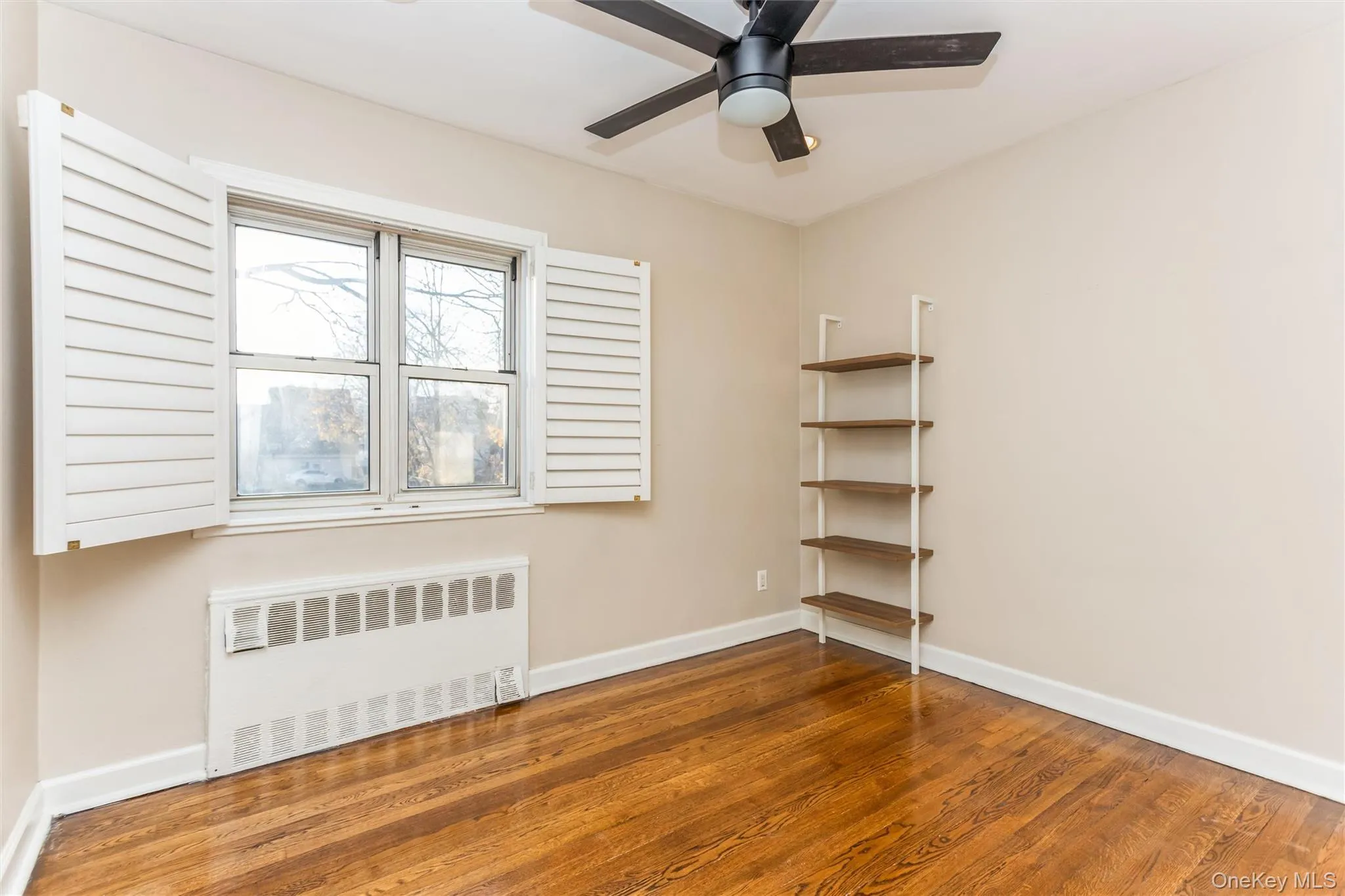 Empty room with radiator, wood finished floors, and ceiling fan Empty room with radiator, wood finished floors, and ceiling fan