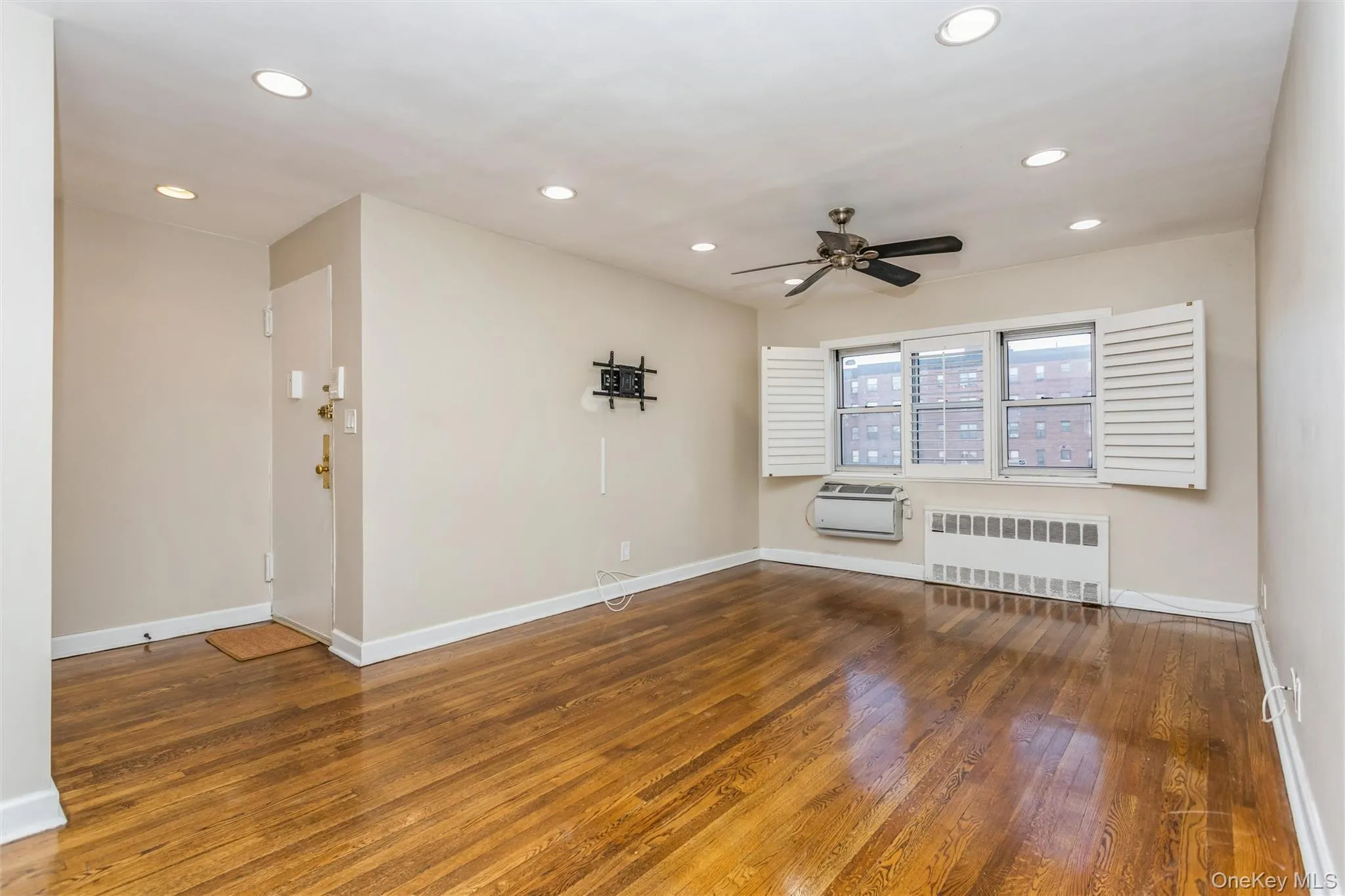 Empty room with hardwood / wood-style floors, radiator, recessed lighting, ceiling fan, and an AC wall unit Empty room with hardwood / wood-style floors, radiator, recessed lighting, ceiling fan, and an AC wall unit