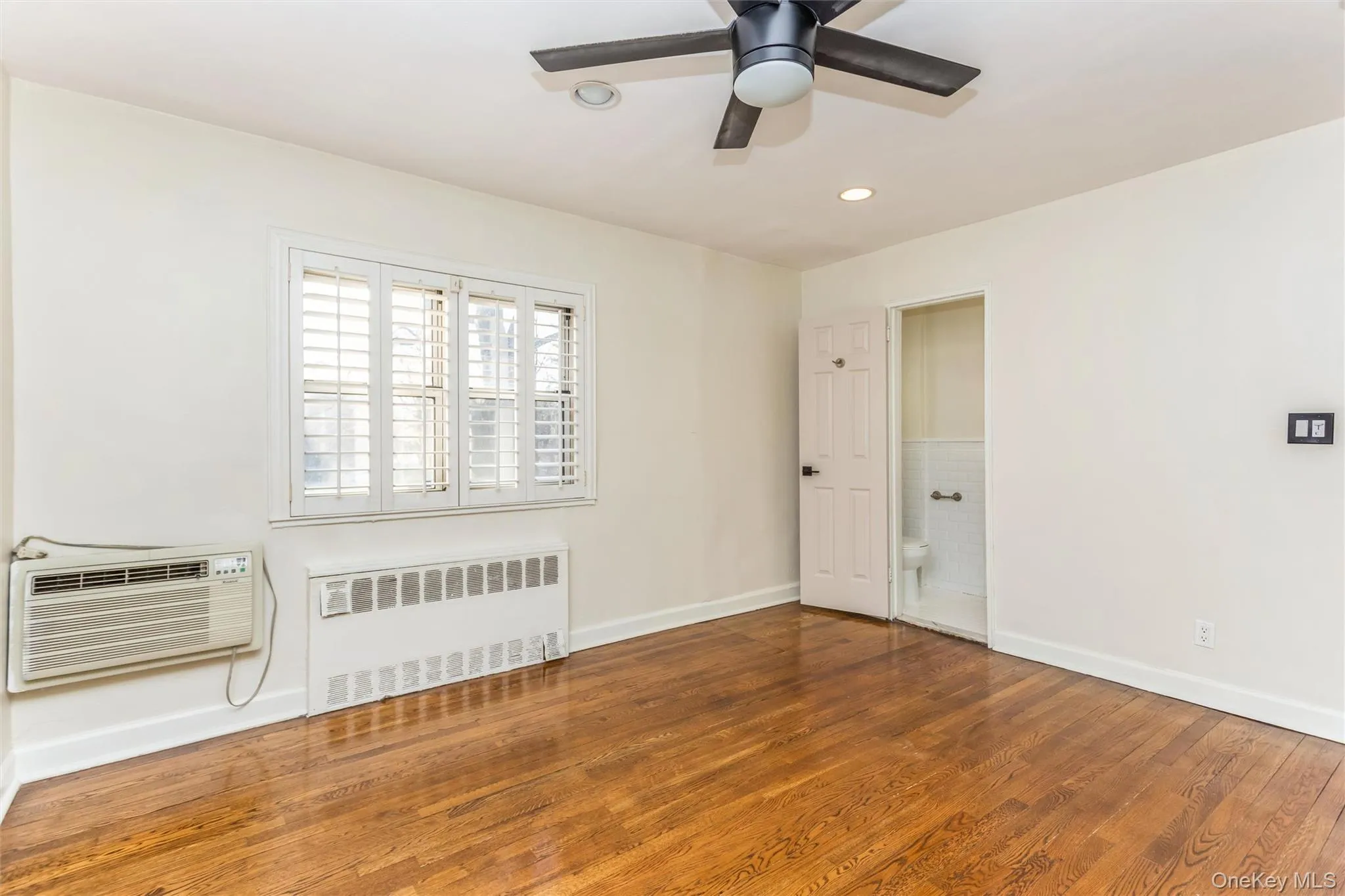 Empty room featuring radiator heating unit, wood finished floors, a wall unit AC, recessed lighting, and ceiling fan Empty room featuring radiator heating unit, wood finished floors, a wall unit AC, recessed lighting, and ceiling fan