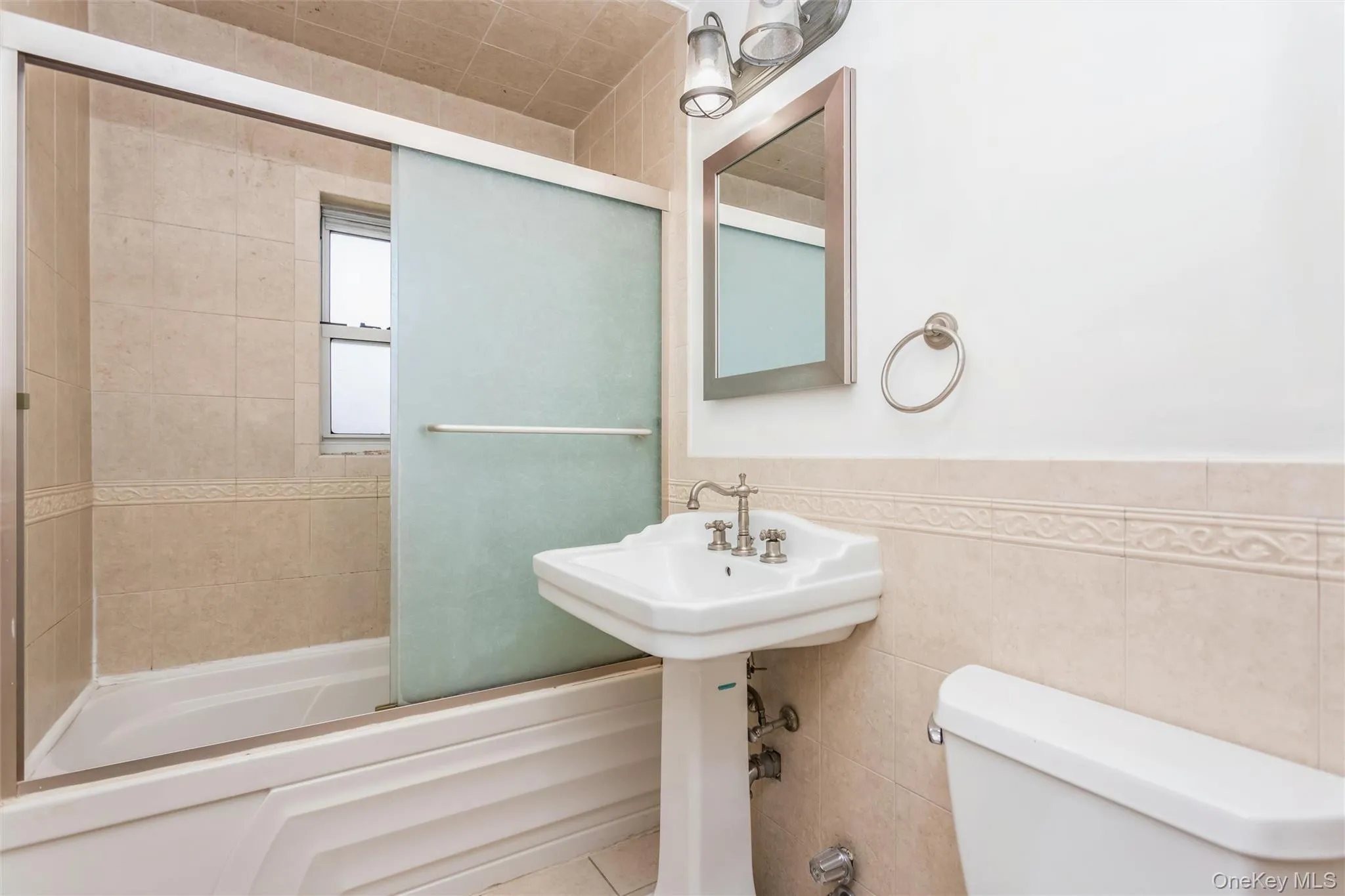 Bathroom with bath / shower combo with glass door, tile walls, a wainscoted wall, and tile patterned flooring Bathroom with bath / shower combo with glass door, tile walls, a wainscoted wall, and tile patterned flooring