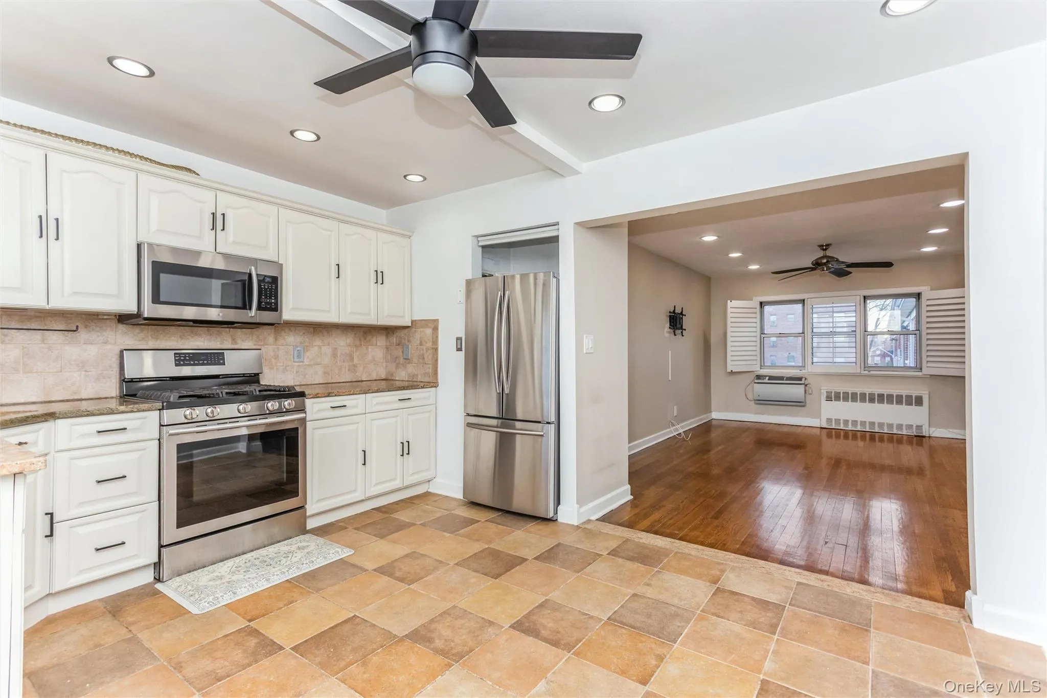 Kitchen featuring ceiling fan, appliances with stainless steel finishes, tasteful backsplash, radiator, and light stone counters Kitchen featuring ceiling fan, appliances with stainless steel finishes, tasteful backsplash, radiator, and light stone counters