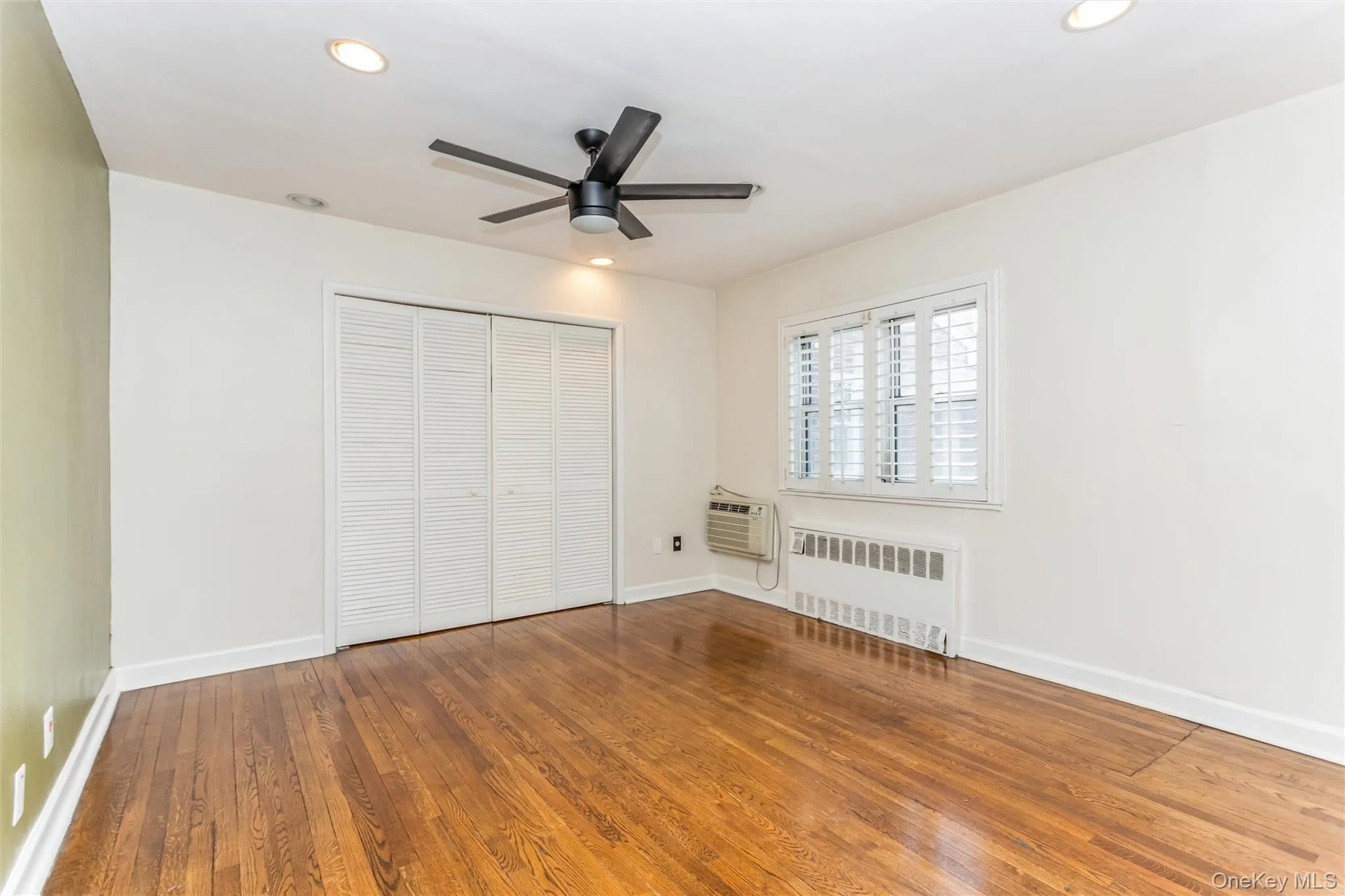 Unfurnished bedroom with radiator, wood finished floors, ceiling fan, recessed lighting, and a closet Unfurnished bedroom with radiator, wood finished floors, ceiling fan, recessed lighting, and a closet
