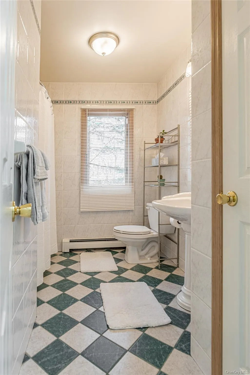 Bathroom with tile walls, a shower with curtain, and a baseboard heating unit Bathroom with tile walls, a shower with curtain, and a baseboard heating unit
