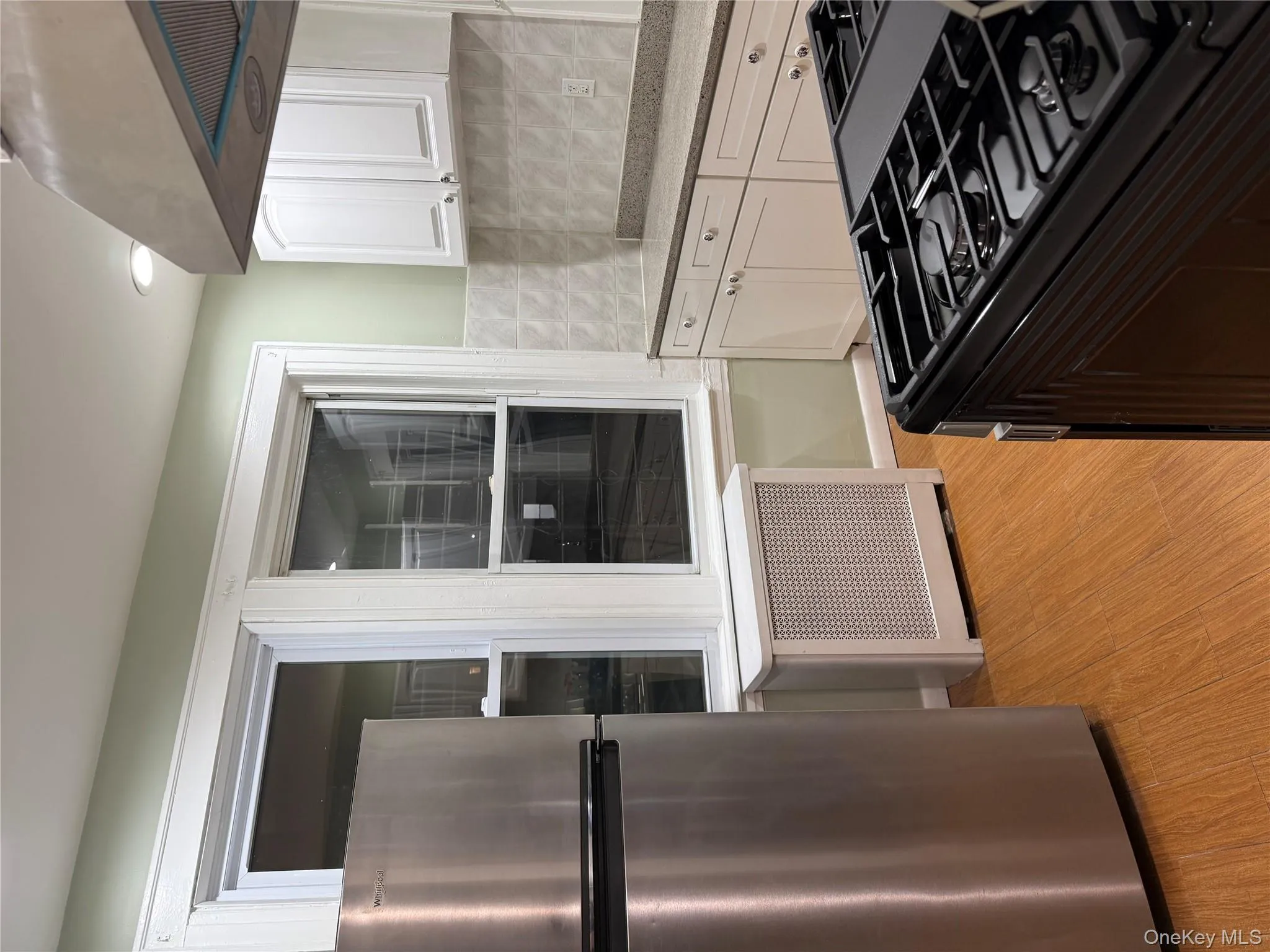Kitchen featuring refrigerator, white cabinetry, stainless steel stove, radiator heating unit, and ventilation hood Kitchen featuring refrigerator, white cabinetry, stainless steel stove, radiator heating unit, and ventilation hood