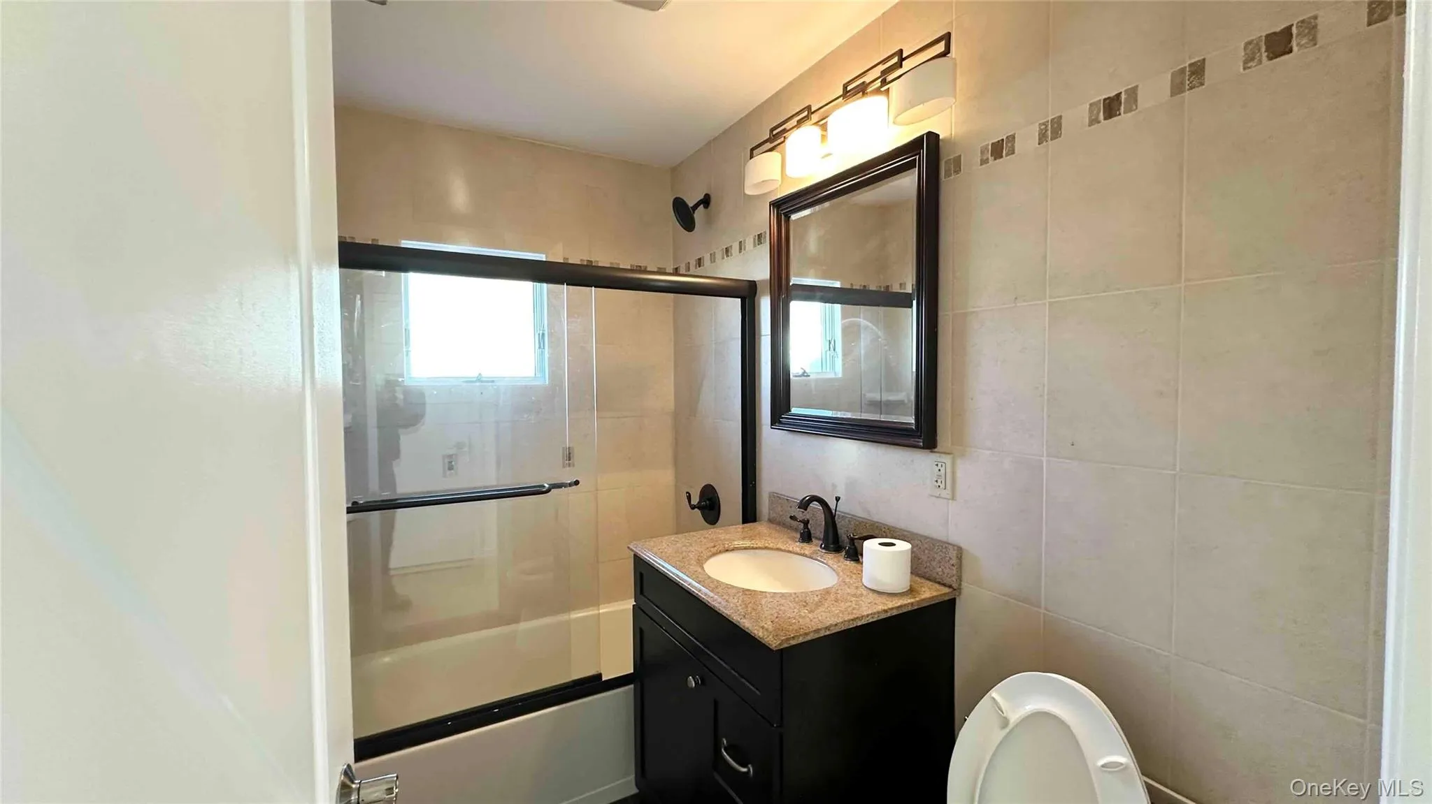 Bathroom featuring vanity, enclosed tub / shower combo, and tile walls Bathroom featuring vanity, enclosed tub / shower combo, and tile walls
