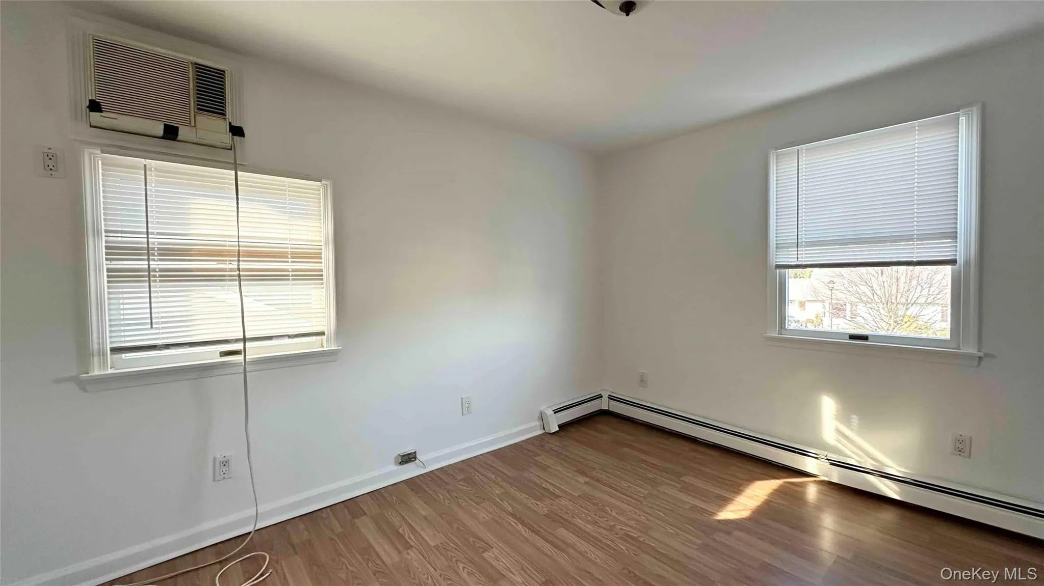 Spare room featuring wood finished floors, a baseboard radiator, an AC wall unit, and healthy amount of natural light Spare room featuring wood finished floors, a baseboard radiator, an AC wall unit, and healthy amount of natural light