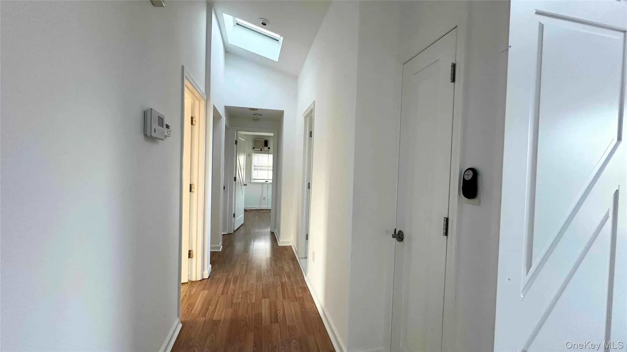 Corridor with dark wood finished floors, vaulted ceiling, and a skylight Corridor with dark wood finished floors, vaulted ceiling, and a skylight