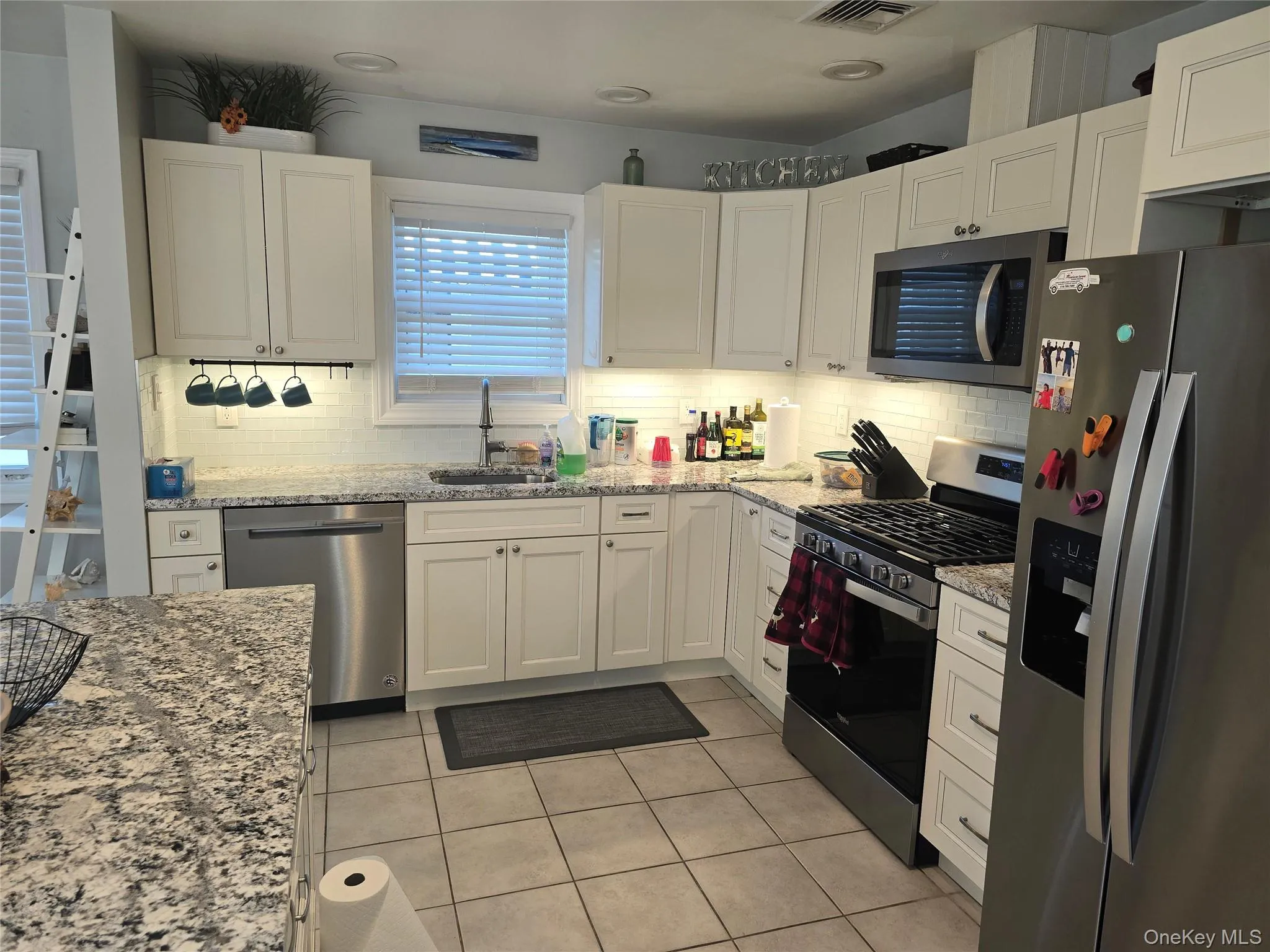 Kitchen featuring stainless steel appliances, light stone counters, white cabinets, and light tile patterned flooring Kitchen featuring stainless steel appliances, light stone counters, white cabinets, and light tile patterned flooring