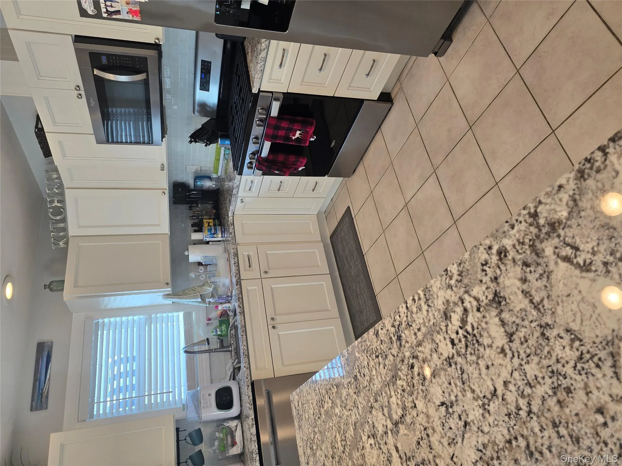 Kitchen with stove, light stone countertops, refrigerator, white cabinetry, and backsplash Kitchen with stove, light stone countertops, refrigerator, white cabinetry, and backsplash