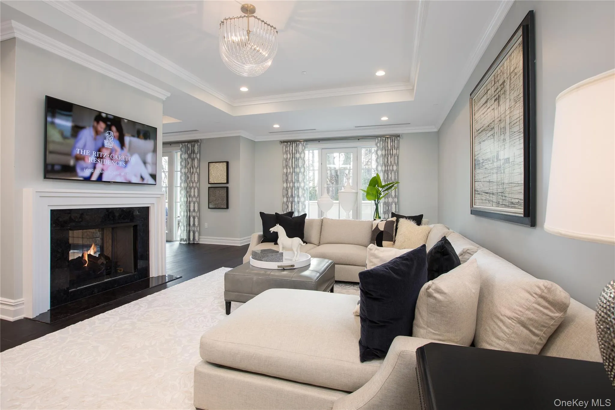 Living area with a raised ceiling, recessed lighting, crown molding, a premium fireplace, and wood finished floors Living area with a raised ceiling, recessed lighting, crown molding, a premium fireplace, and wood finished floors