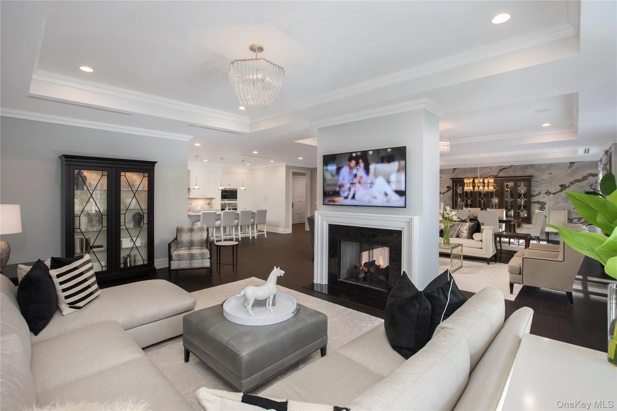 Living room with a raised ceiling, a chandelier, recessed lighting, a multi sided fireplace, and wood finished floors Living room with a raised ceiling, a chandelier, recessed lighting, a multi sided fireplace, and wood finished floors