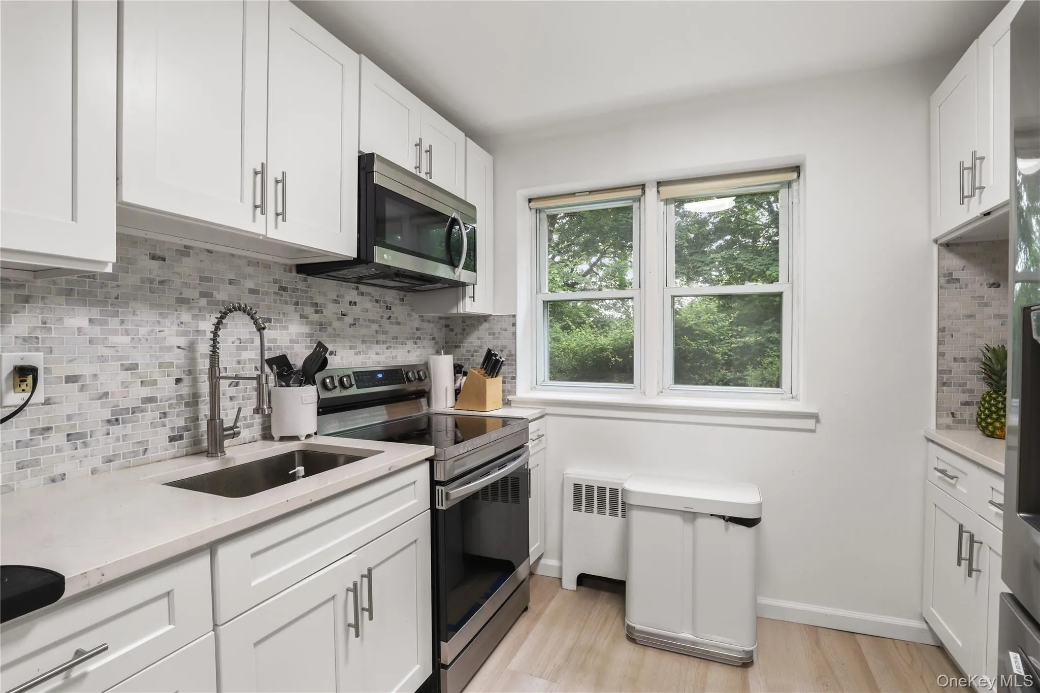 Kitchen featuring appliances with stainless steel finishes, light countertops, white cabinetry, radiator heating unit, and light wood-style flooring Kitchen featuring appliances with stainless steel finishes, light countertops, white cabinetry, radiator heating unit, and light wood-style flooring