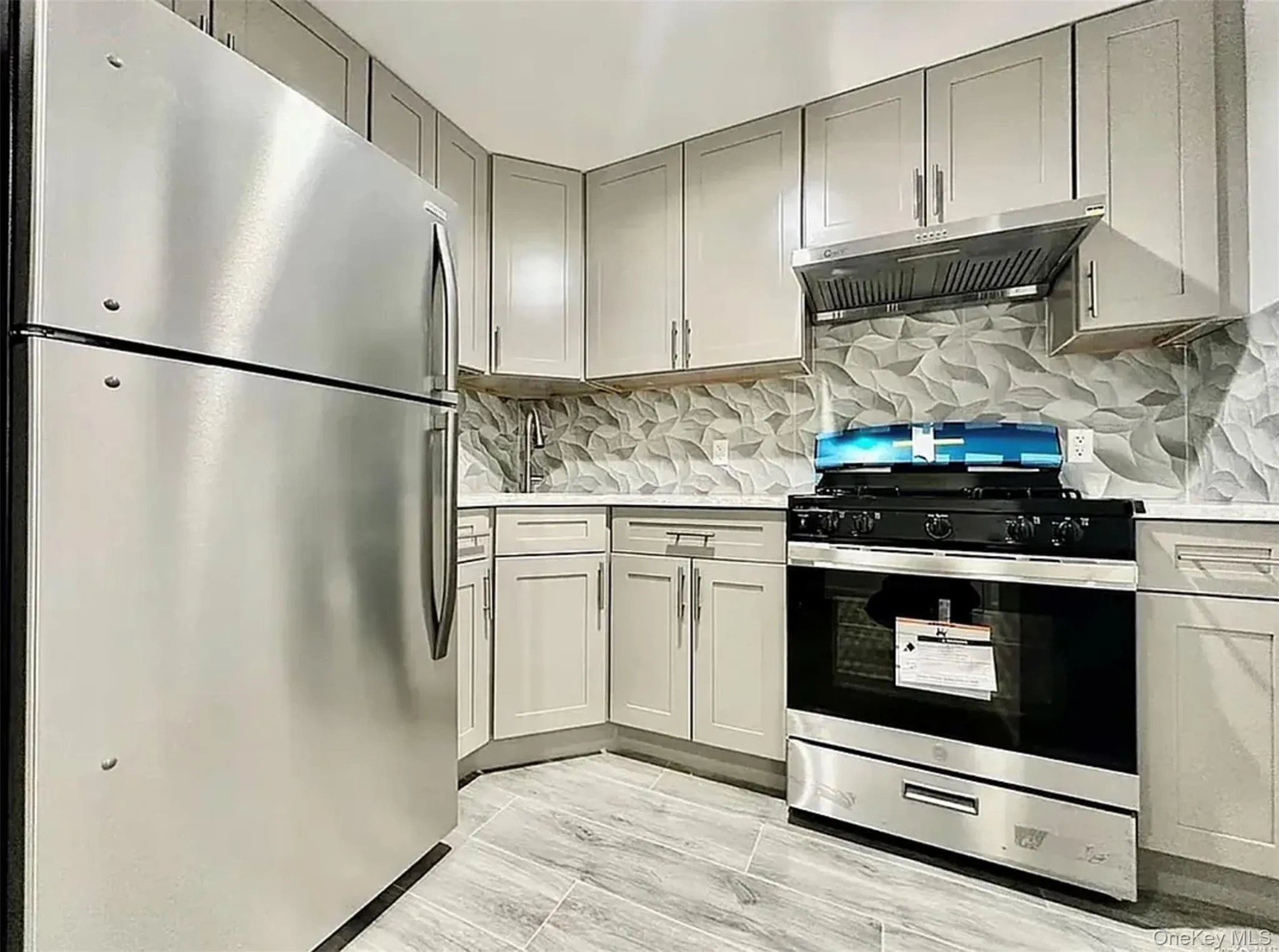 Kitchen featuring stainless steel appliances, exhaust hood, tasteful backsplash, and light stone counters Kitchen featuring stainless steel appliances, exhaust hood, tasteful backsplash, and light stone counters