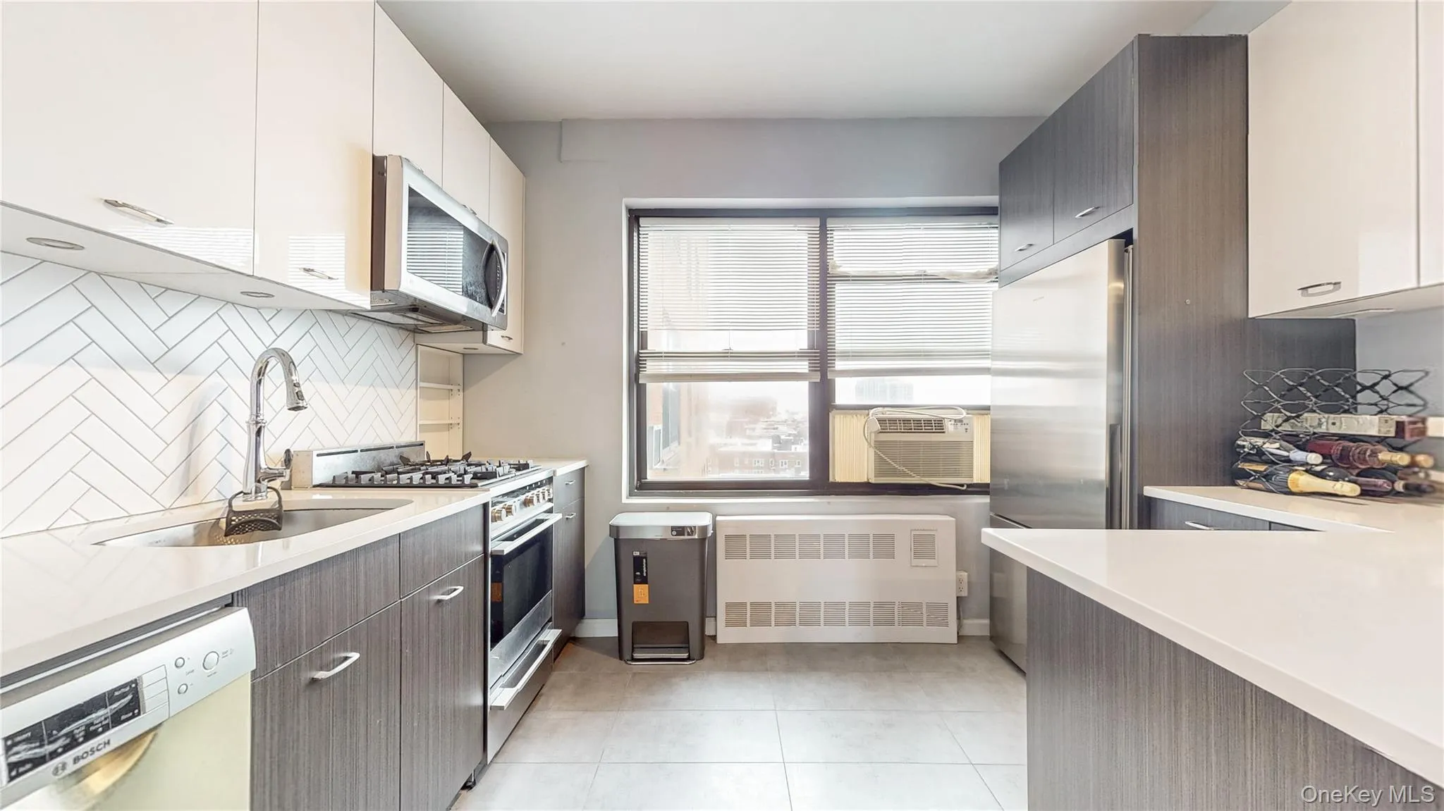 Windowed Kitchen with appliances with stainless steel finishes, radiator, decorative backsplash, light stone counters, and light tile patterned flooring Windowed Kitchen with appliances with stainless steel finishes, radiator, decorative backsplash, light stone counters, and light tile patterned flooring