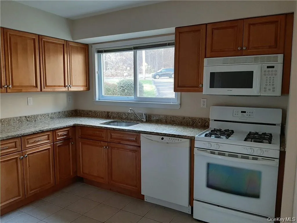 Kitchen featuring white appliances, brown cabinets, light stone countertops, and light tile patterned floors Kitchen featuring white appliances, brown cabinets, light stone countertops, and light tile patterned floors