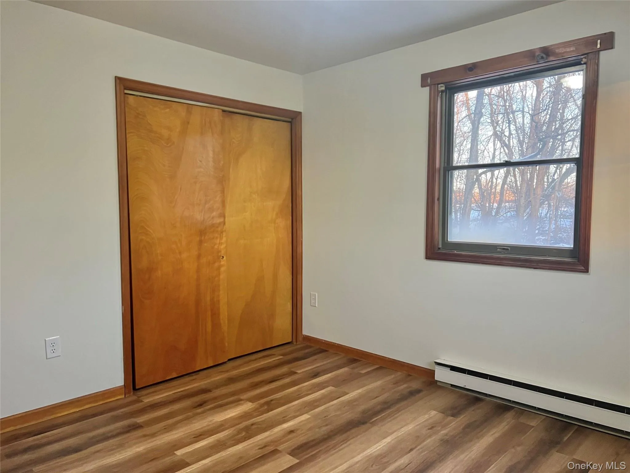 Unfurnished bedroom featuring a baseboard heating unit, wood finished floors, and a closet Unfurnished bedroom featuring a baseboard heating unit, wood finished floors, and a closet