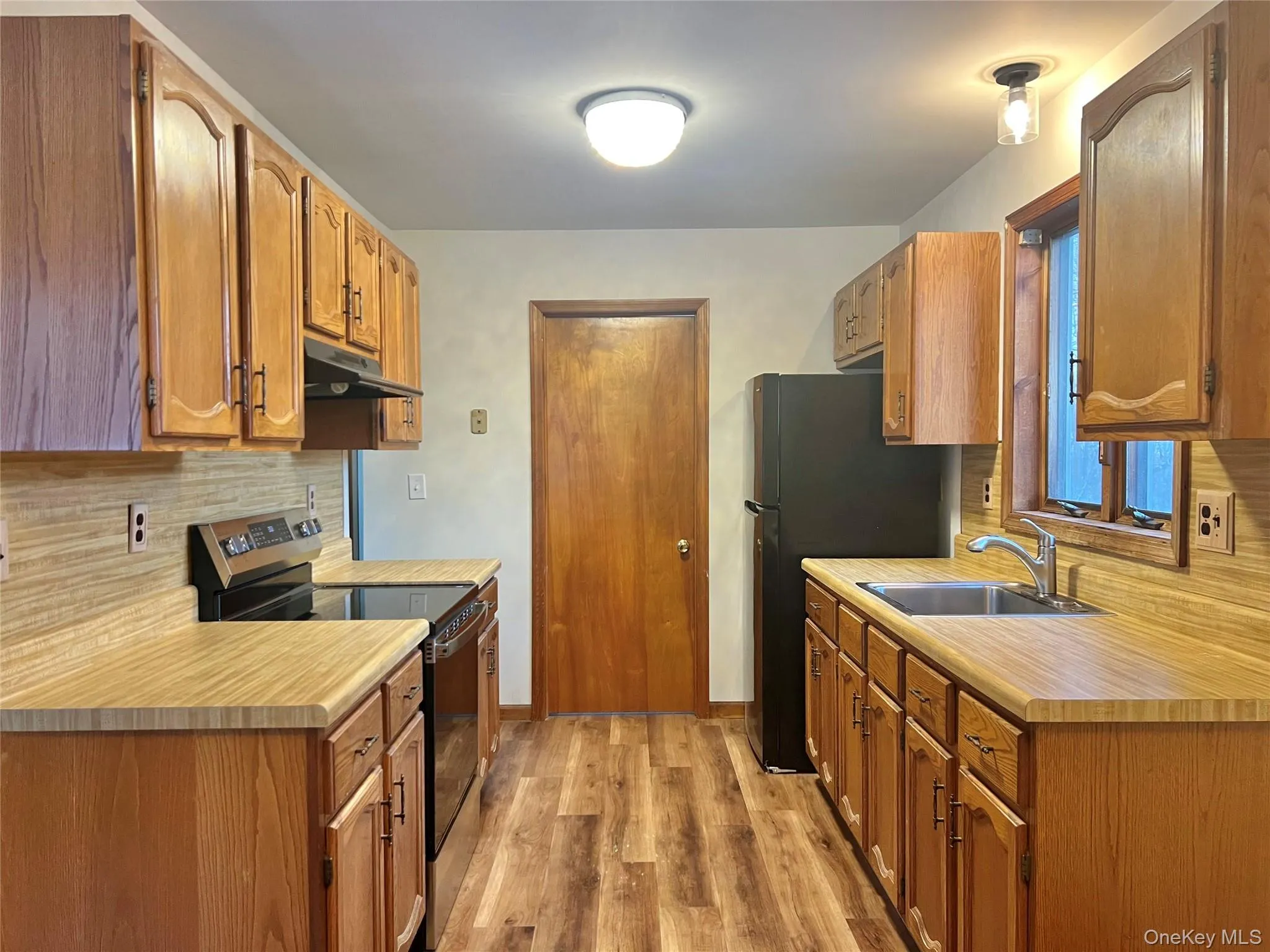 Kitchen featuring stainless steel range with electric cooktop, decorative backsplash, light countertops, and light wood-style flooring Kitchen featuring stainless steel range with electric cooktop, decorative backsplash, light countertops, and light wood-style flooring