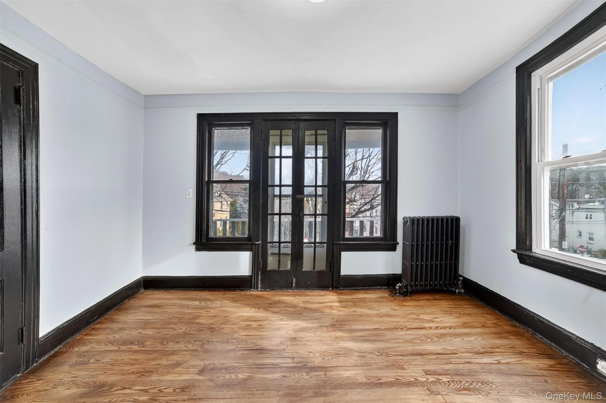 Empty room featuring wood finished floors, radiator, and french doors Empty room featuring wood finished floors, radiator, and french doors