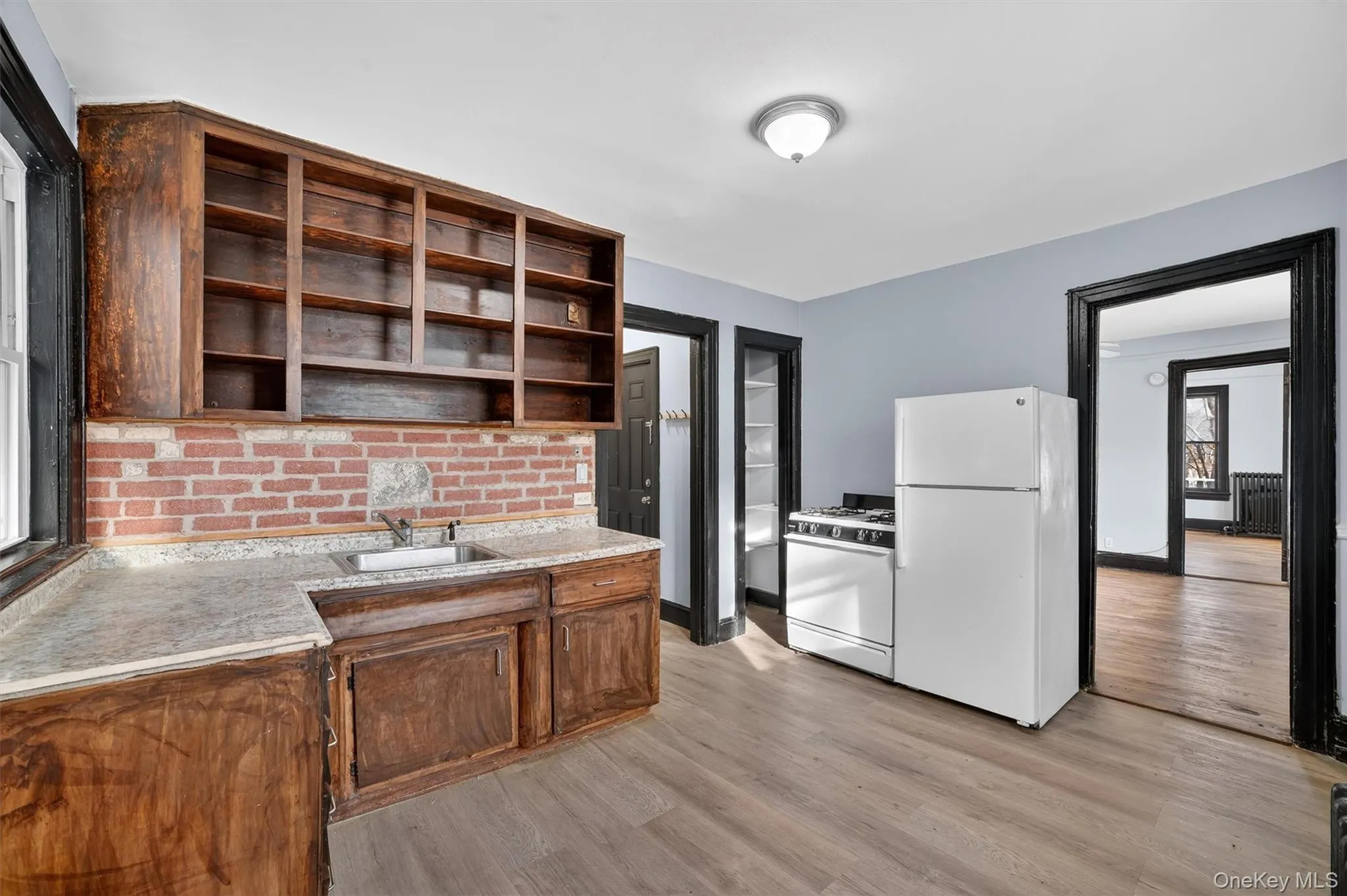 Kitchen featuring white appliances, light wood-style floors, open shelves, radiator heating unit, and light stone counters Kitchen featuring white appliances, light wood-style floors, open shelves, radiator heating unit, and light stone counters