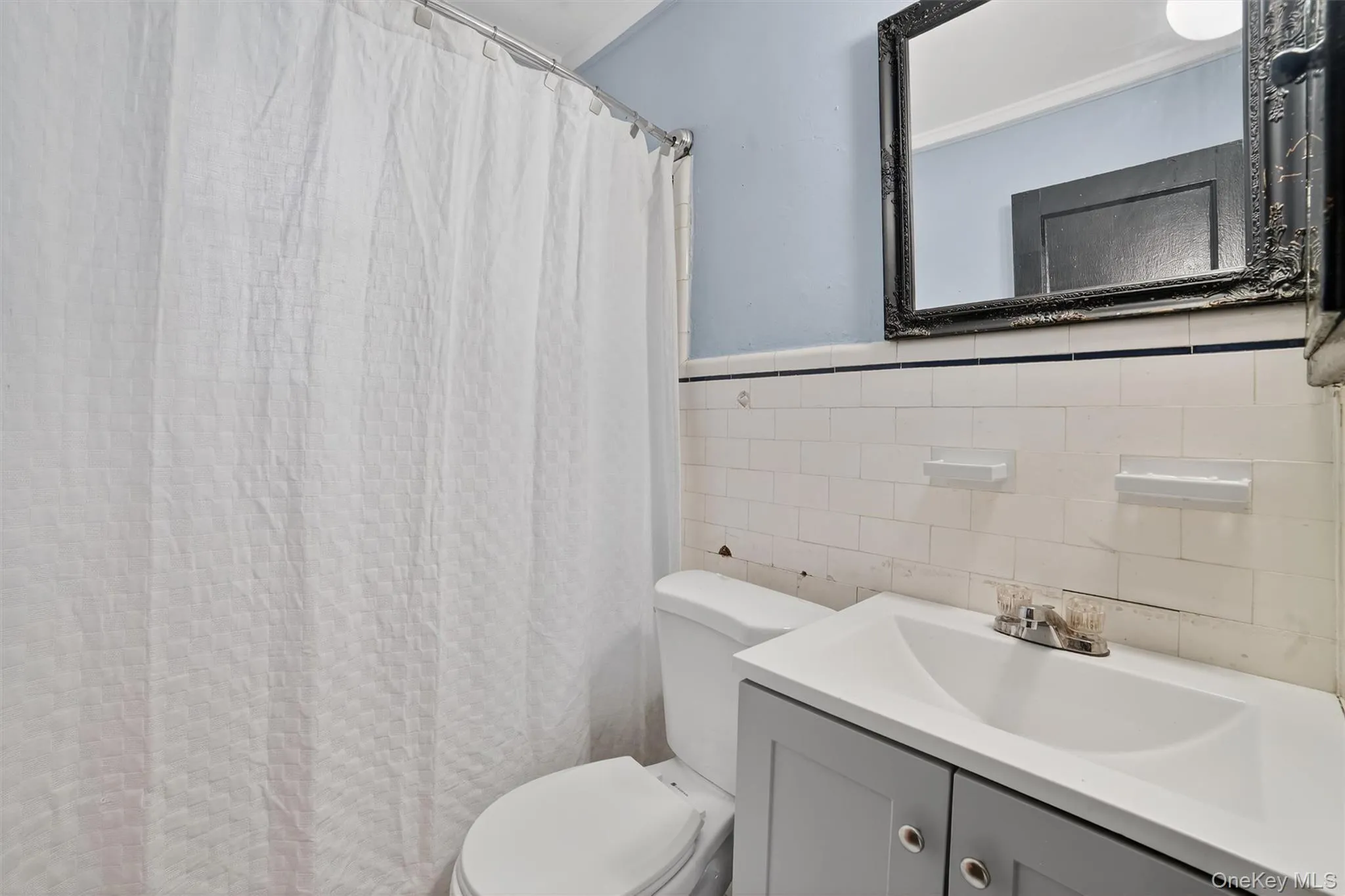 Full bathroom with tile walls, vanity, a shower with shower curtain, and wainscoting Full bathroom with tile walls, vanity, a shower with shower curtain, and wainscoting