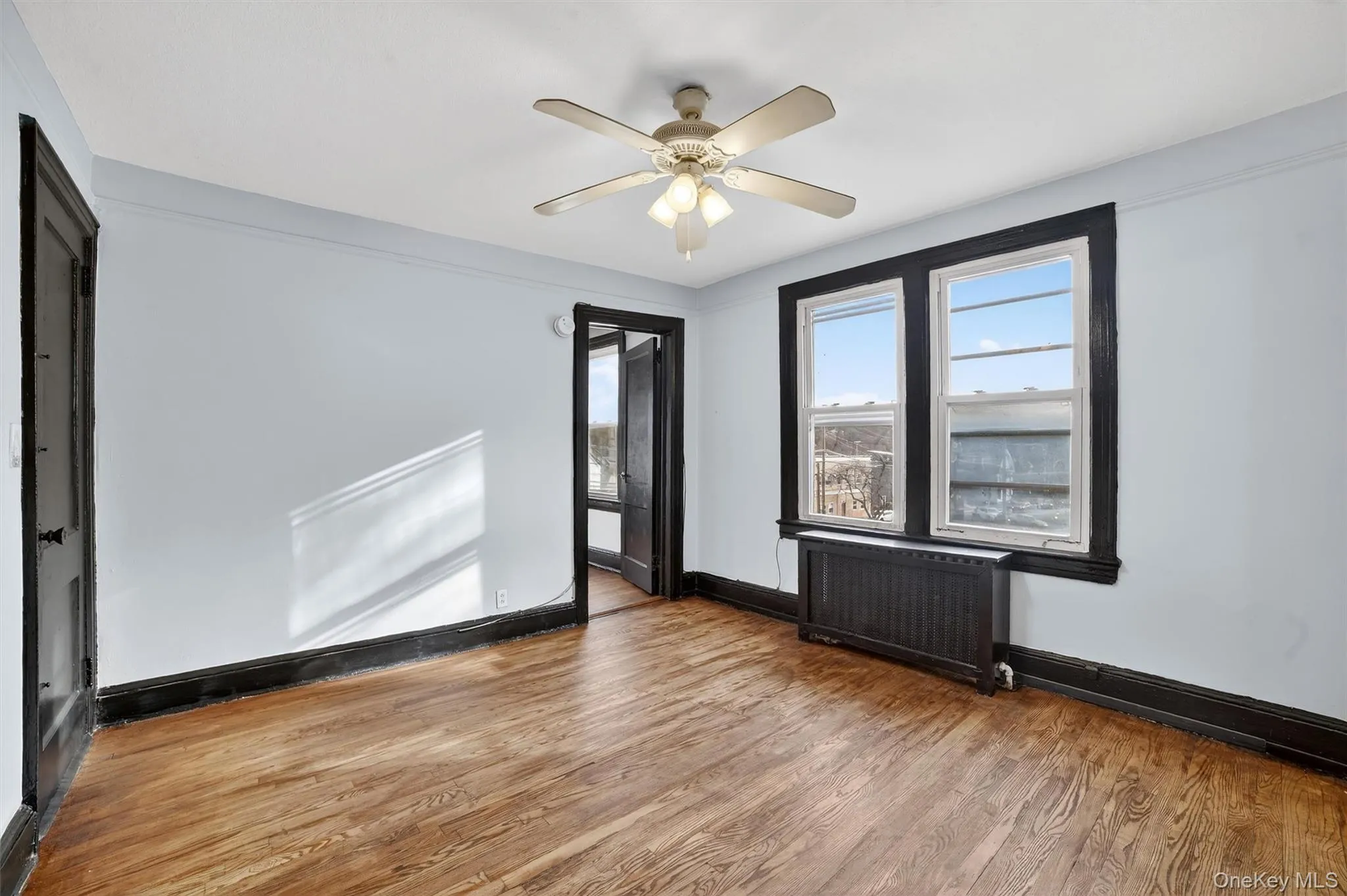 Empty room with radiator heating unit, wood finished floors, and ceiling fan Empty room with radiator heating unit, wood finished floors, and ceiling fan