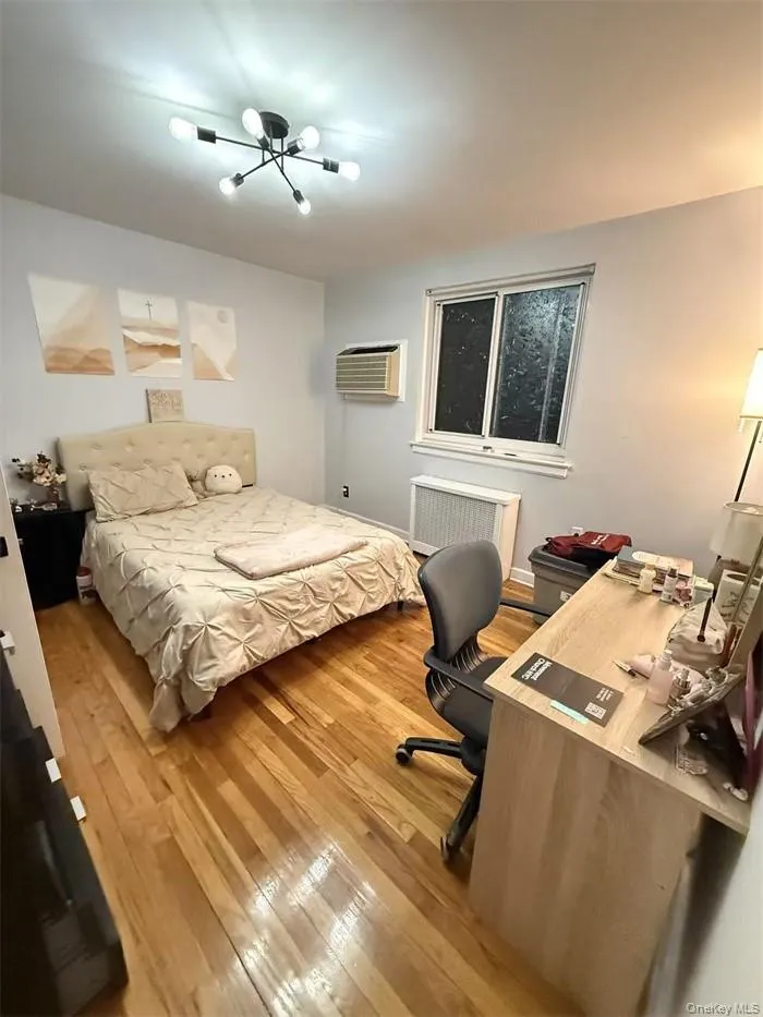 Bedroom featuring a desk, light wood-type flooring, an AC wall unit, and radiator Bedroom featuring a desk, light wood-type flooring, an AC wall unit, and radiator