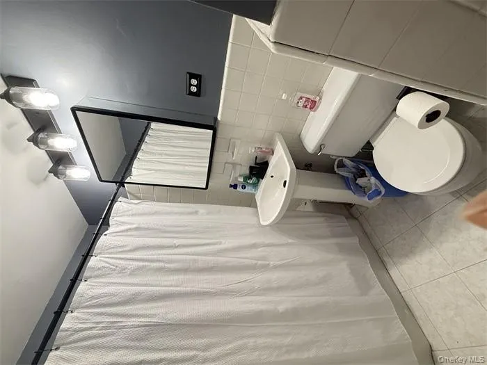 Full bathroom featuring tile walls, a shower with shower curtain, and light tile patterned floors Full bathroom featuring tile walls, a shower with shower curtain, and light tile patterned floors