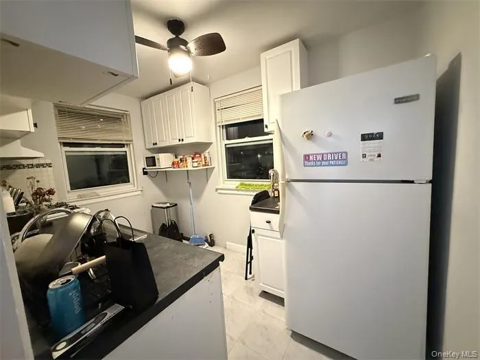 Kitchen featuring freestanding refrigerator, white cabinetry, open shelves, ceiling fan, and dark countertops Kitchen featuring freestanding refrigerator, white cabinetry, open shelves, ceiling fan, and dark countertops