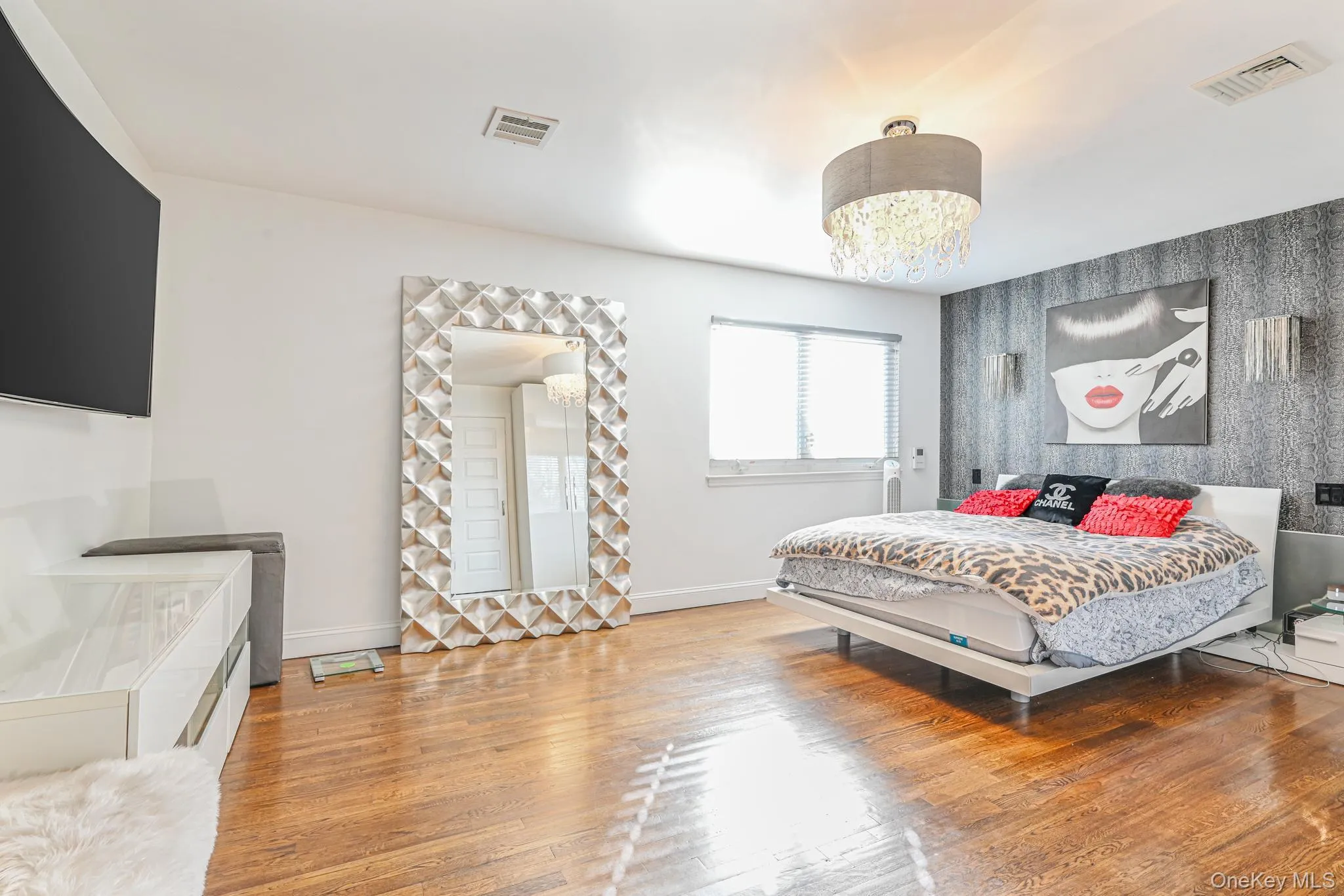 Bedroom featuring light wood-type flooring, a chandelier, and an accent wall Bedroom featuring light wood-type flooring, a chandelier, and an accent wall