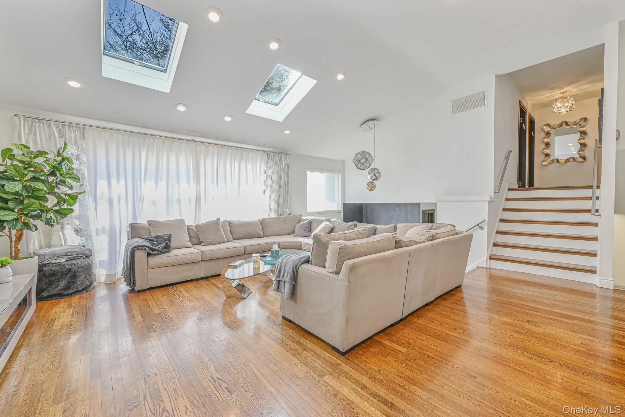 Living room with stairs, light wood-style floors, vaulted ceiling, and a skylight Living room with stairs, light wood-style floors, vaulted ceiling, and a skylight