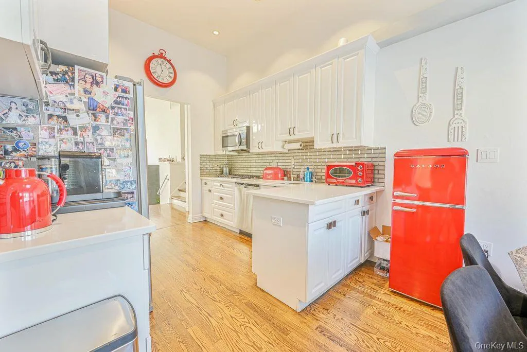 Kitchen with white cabinetry, stainless steel appliances, decorative backsplash, light wood-style flooring, and a peninsula Kitchen with white cabinetry, stainless steel appliances, decorative backsplash, light wood-style flooring, and a peninsula