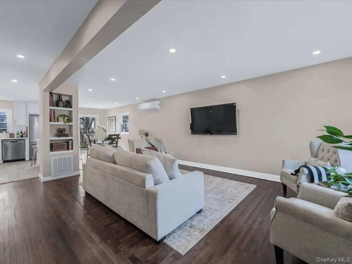 Living room with built in features, dark wood-style flooring, recessed lighting, a wall mounted AC, and healthy amount of natural light Living room with built in features, dark wood-style flooring, recessed lighting, a wall mounted AC, and healthy amount of natural light