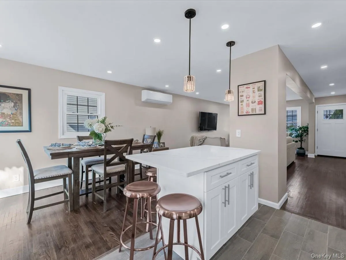 Kitchen with dark wood-style flooring, white cabinets, decorative light fixtures, a center island, and light stone countertops Kitchen with dark wood-style flooring, white cabinets, decorative light fixtures, a center island, and light stone countertops