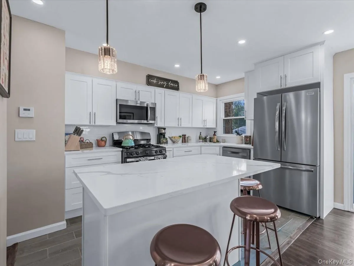 Kitchen with appliances with stainless steel finishes, a breakfast bar, light stone counters, white cabinetry, and recessed lighting Kitchen with appliances with stainless steel finishes, a breakfast bar, light stone counters, white cabinetry, and recessed lighting